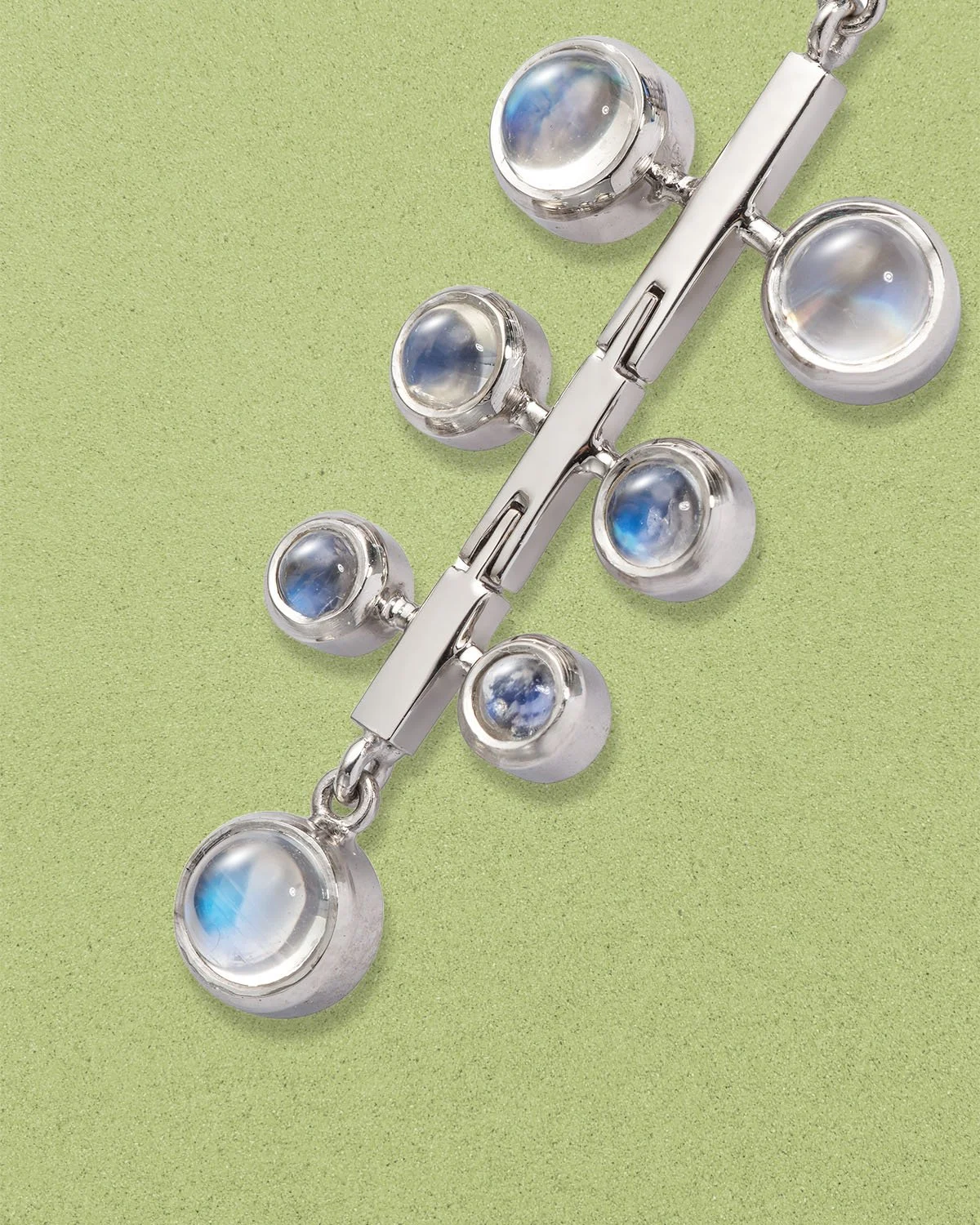 Silver jewellery earring with moonstone cabochons, resting on a green surface.