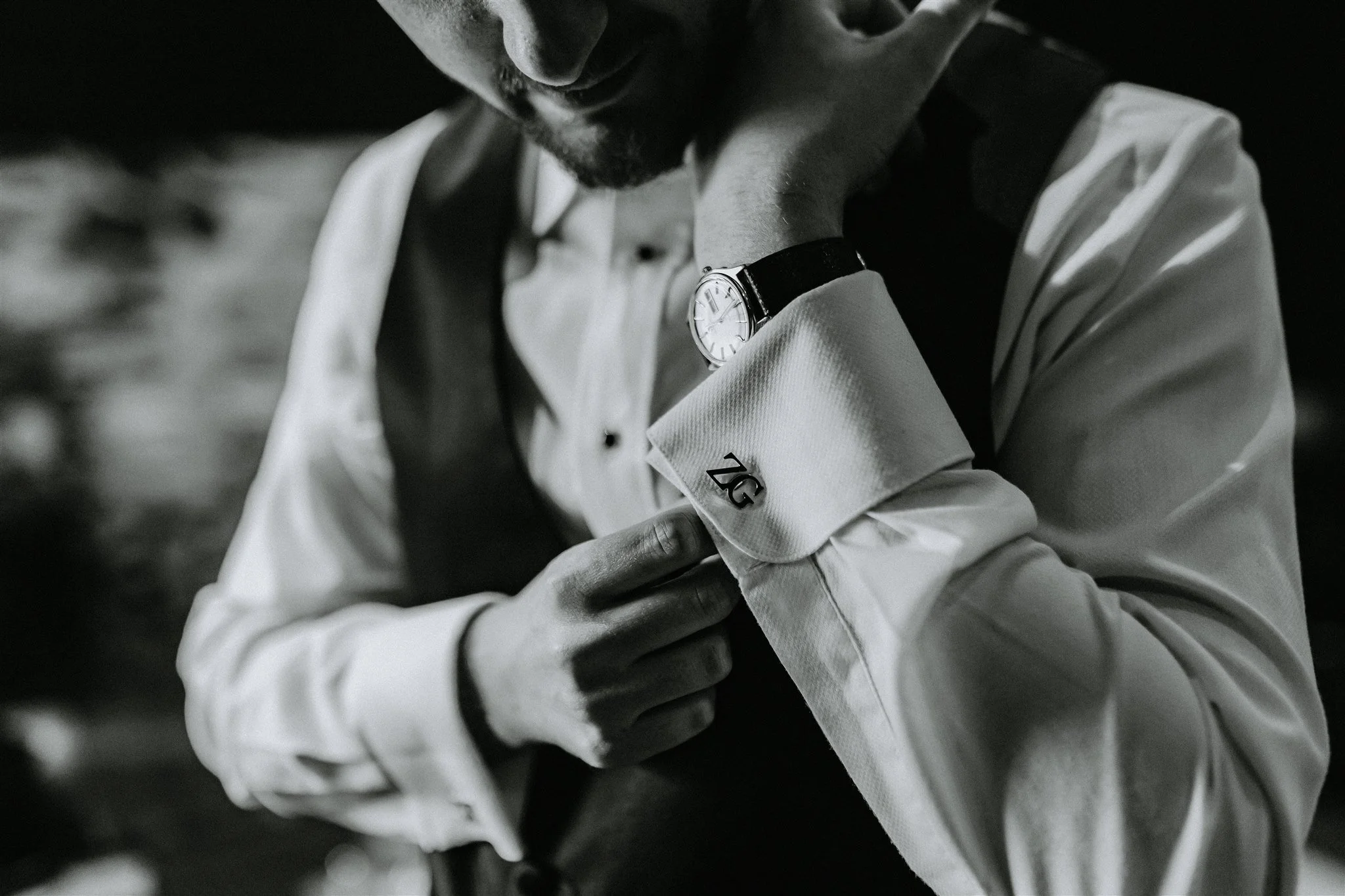 Close-up of a man in a white shirt, looking down thoughtfully, with a watch on his wrist, in a black-and-white photo.