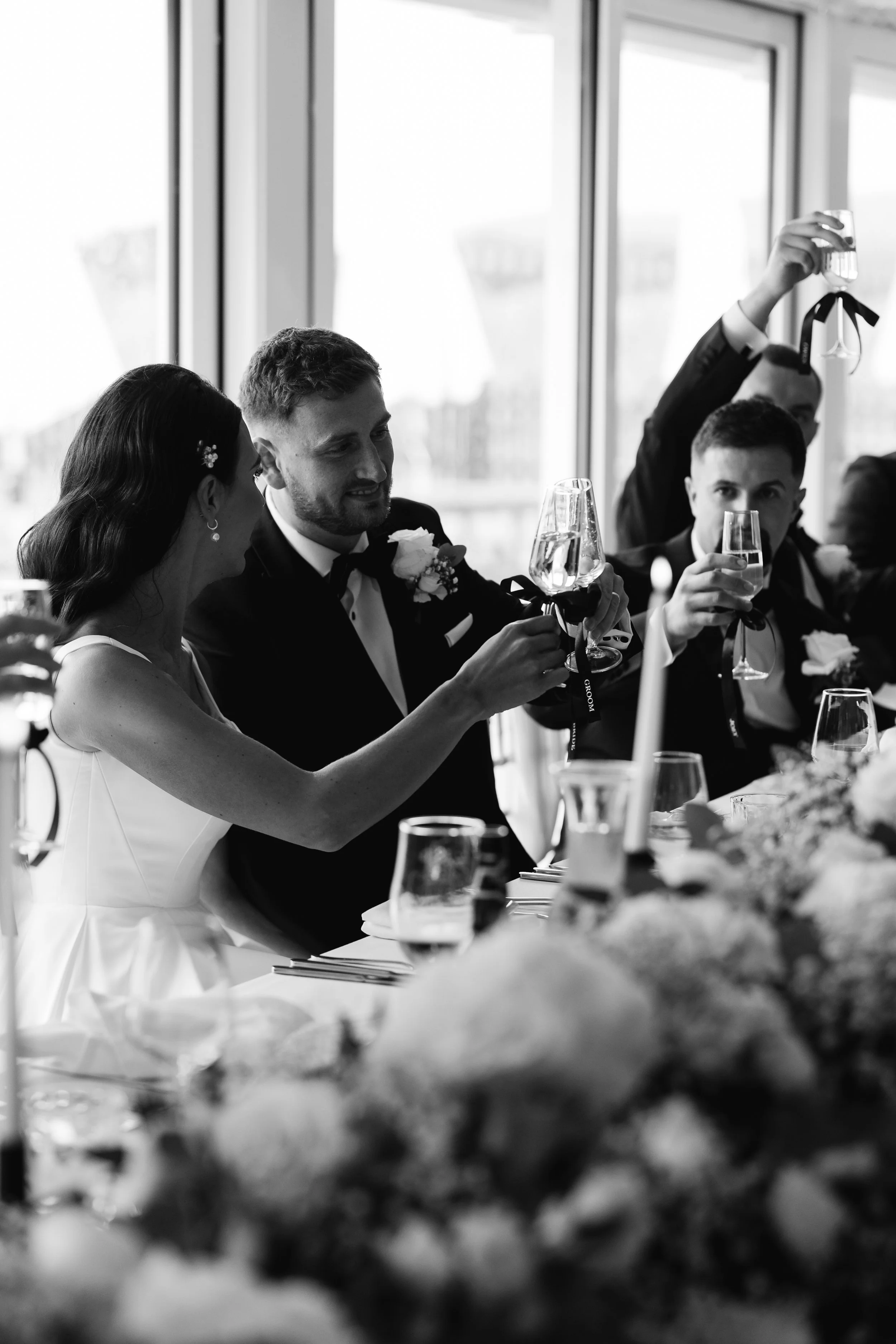 Black and white photo of a wedding reception with a bride, groom, and guests raising glasses for a toast.