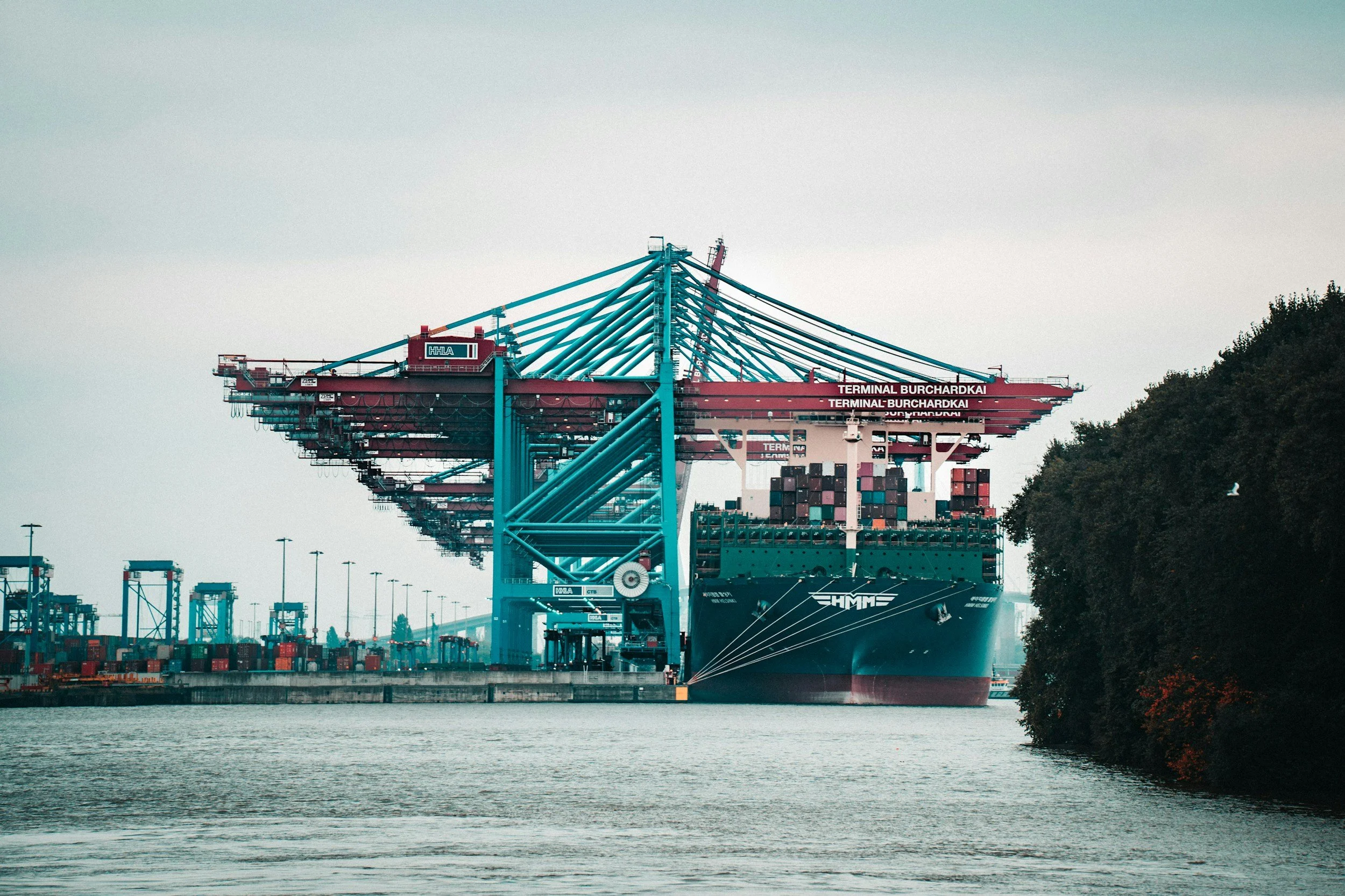A large cargo ship docked at a container terminal with multiple cranes and stacks of shipping containers.