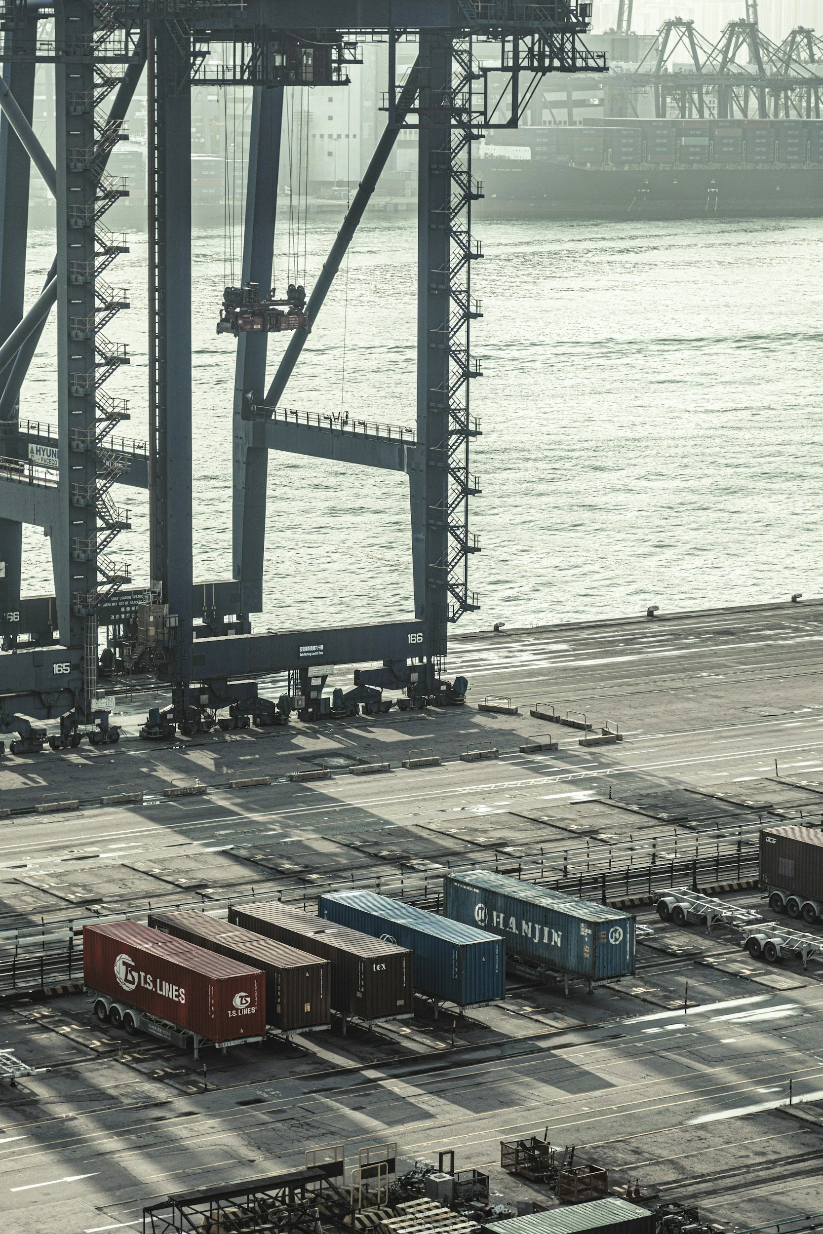 Cargo containers on a shipping dock with a large crane over the water in the background.