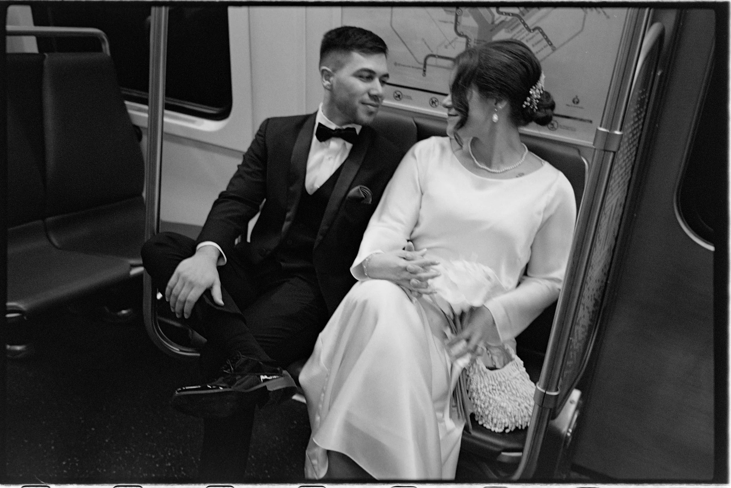 A timeless black and white image of a couple taken the subway train dressed in their bride and groom outfits taken in 35mm film