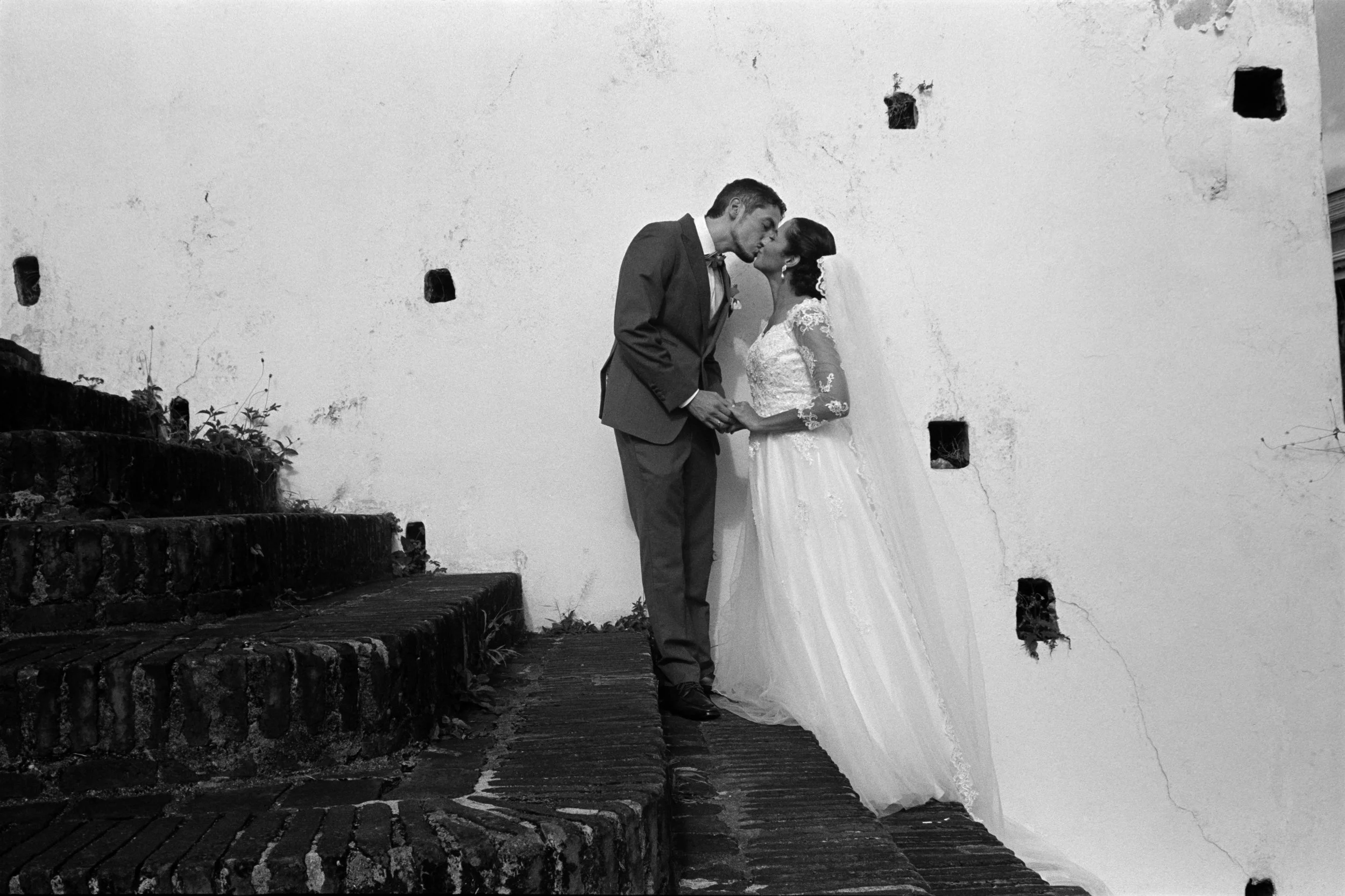 A timeless documentary-style film photo of a bride and groom having their first kiss in Old San Juan, Puerto Rico. With the background showcasing the textured streets of Old San Juan