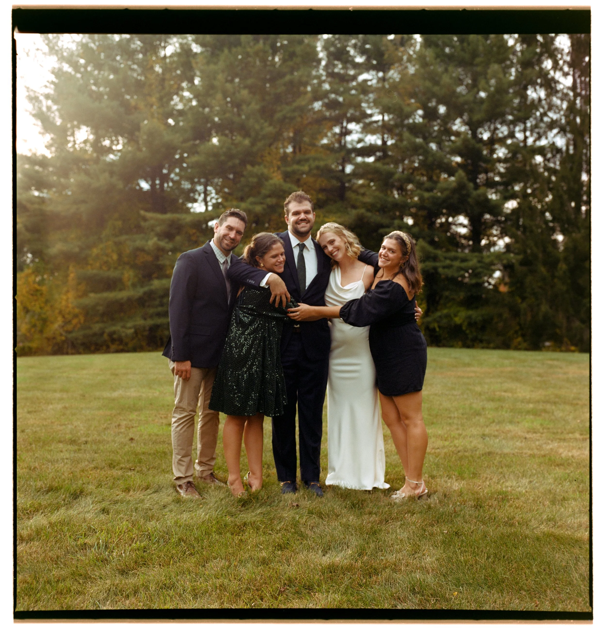 Natural light wedding film photography by a photographer in Puerto Rico using medium format film of friends hugging the bride and groom after getting married