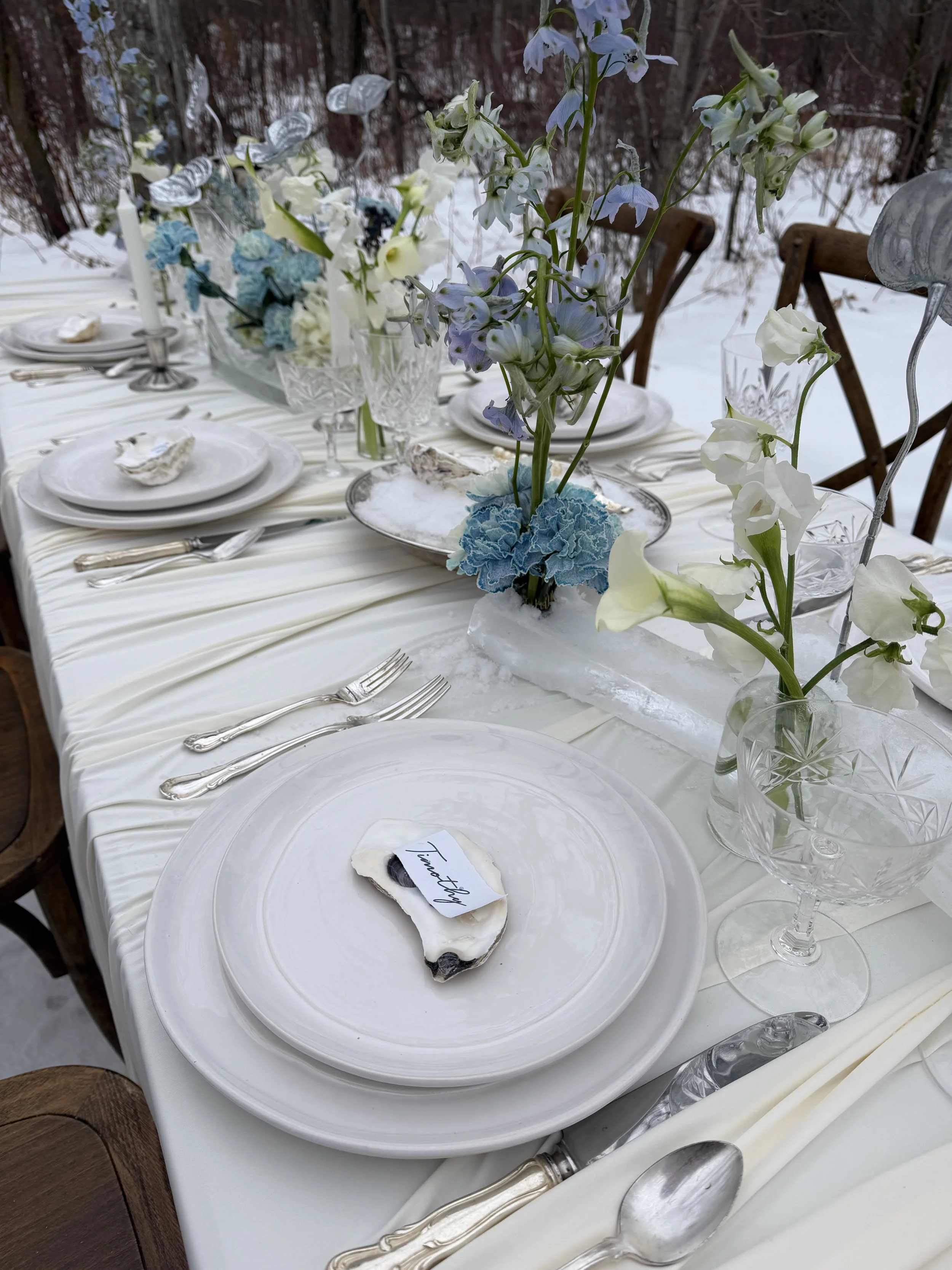 Elegant winter western tablescape with ivory and soft blue floral arrangements, snowy glassware, pearls, oysters, and candles at Sparrow Lane Events.