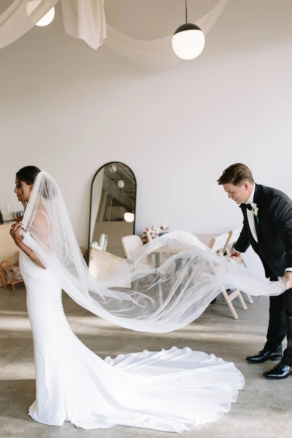 A candid pre-ceremony moment of the groom fixing the bride’s veil, captured naturally before the wedding begins.