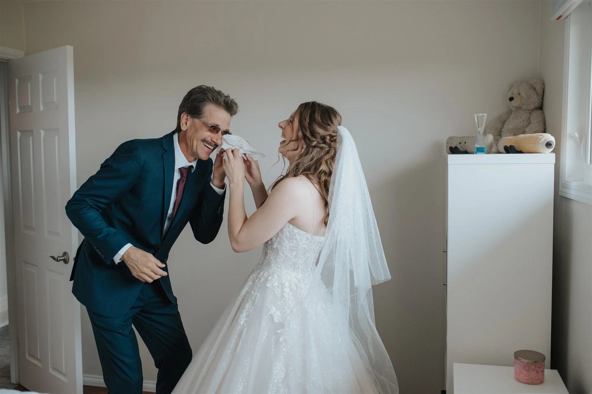 Photograph of bride and the father of the bride laughing and sharing a tissue during first look