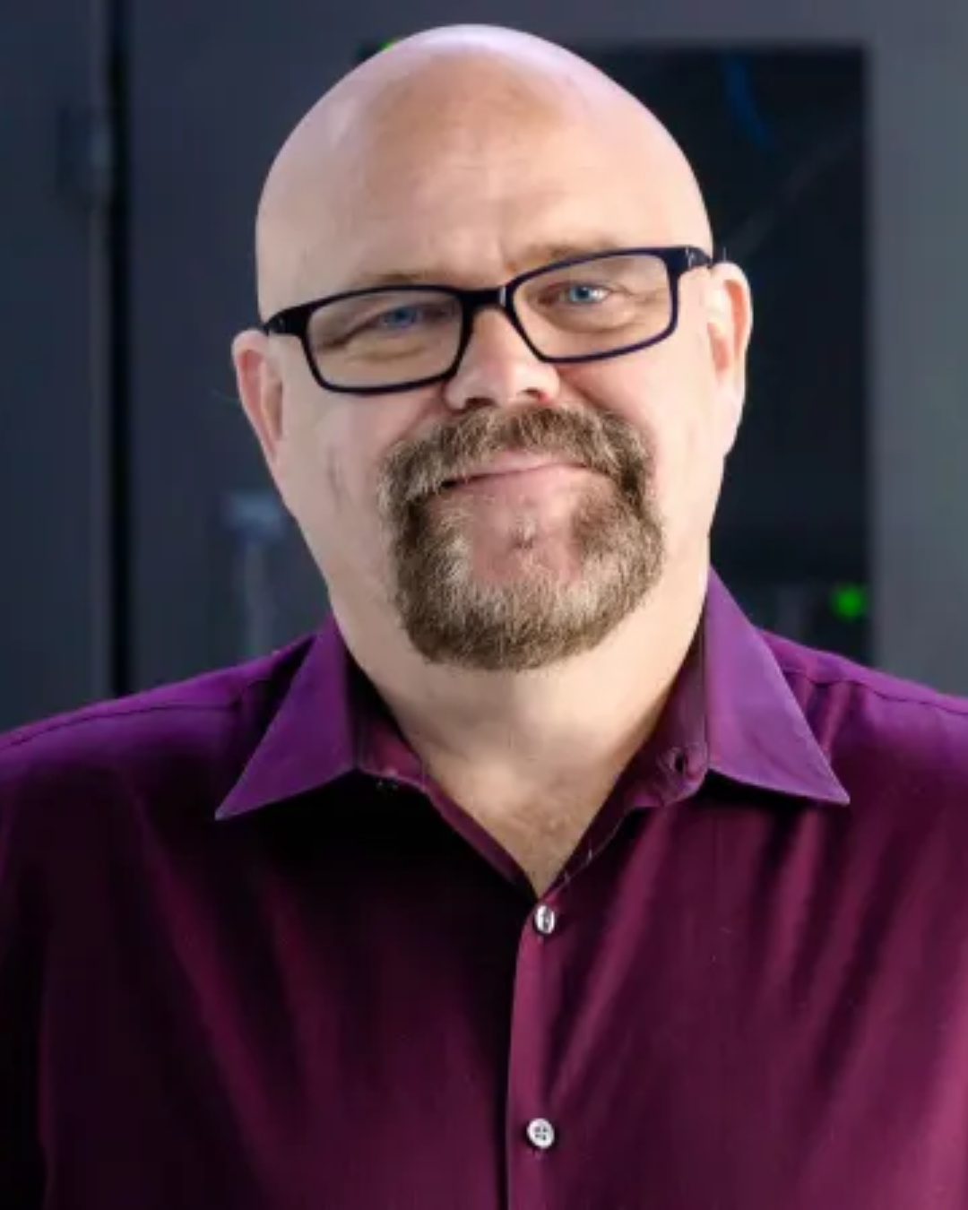 Man in a black shirt standing in a tire warehouse, surrounded by stacked tires.