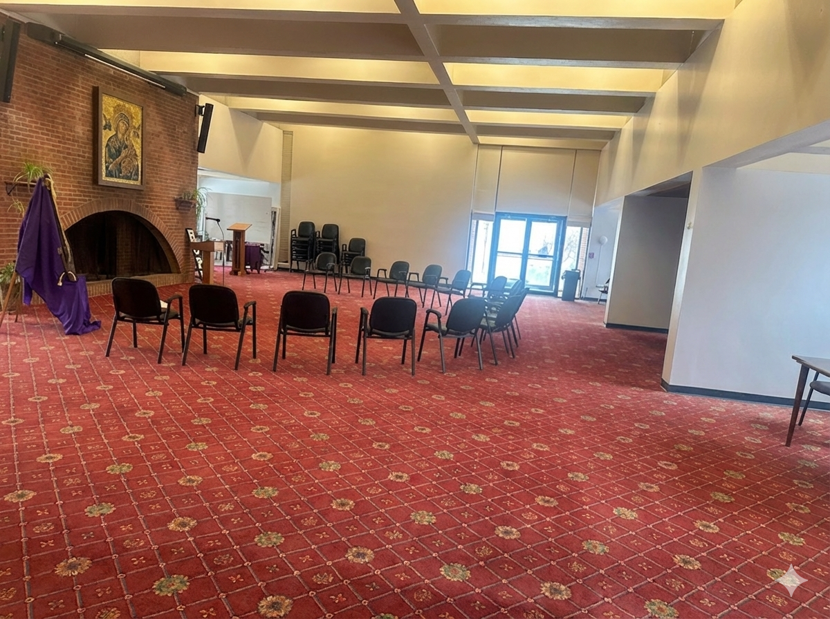 Empty chapel or meeting room with red patterned carpet, black chairs arranged in a semi-circle, brick fireplace with religious icon, purple drapes, and large double glass doors.