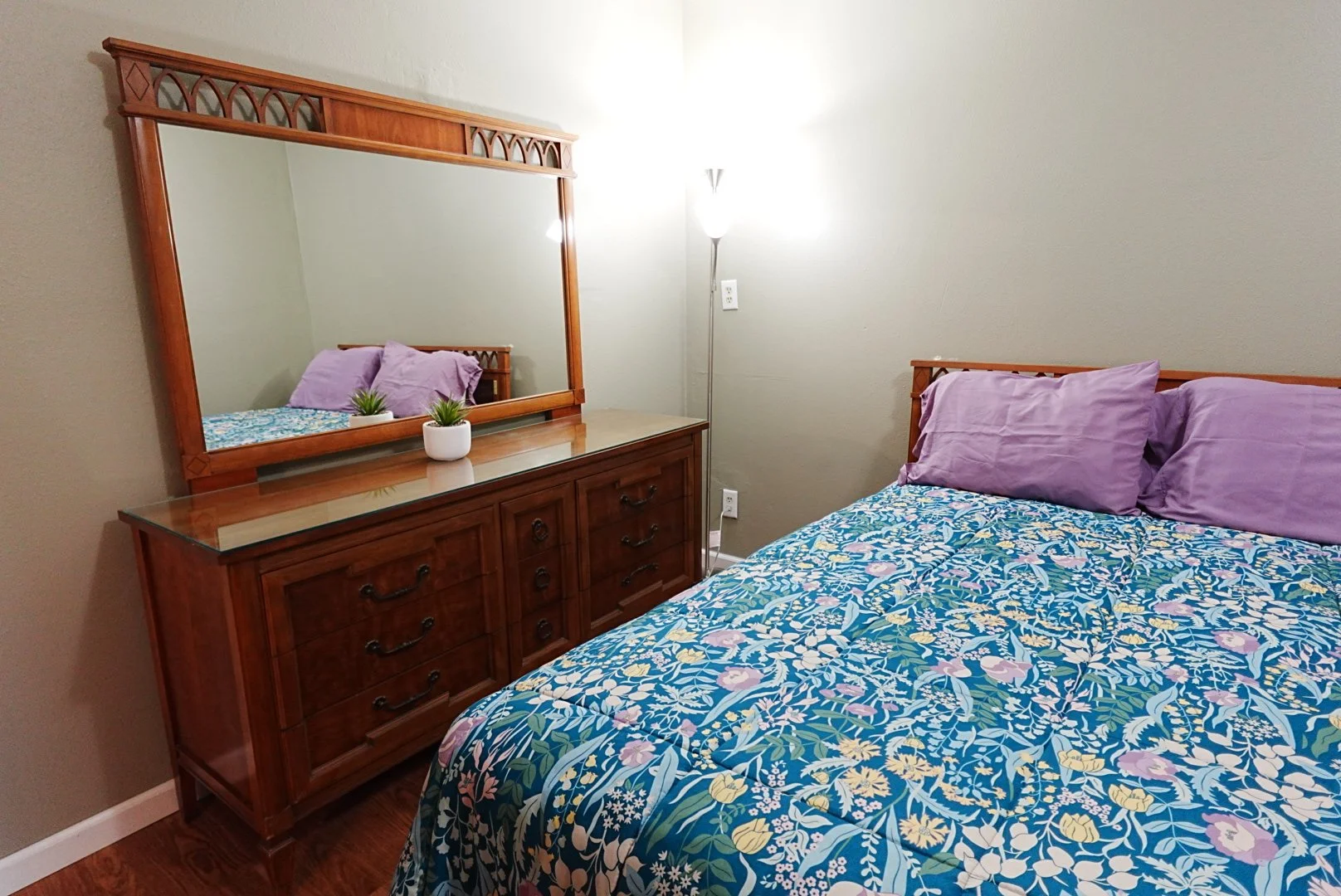 Queen sized bed with dresser and mirror in room