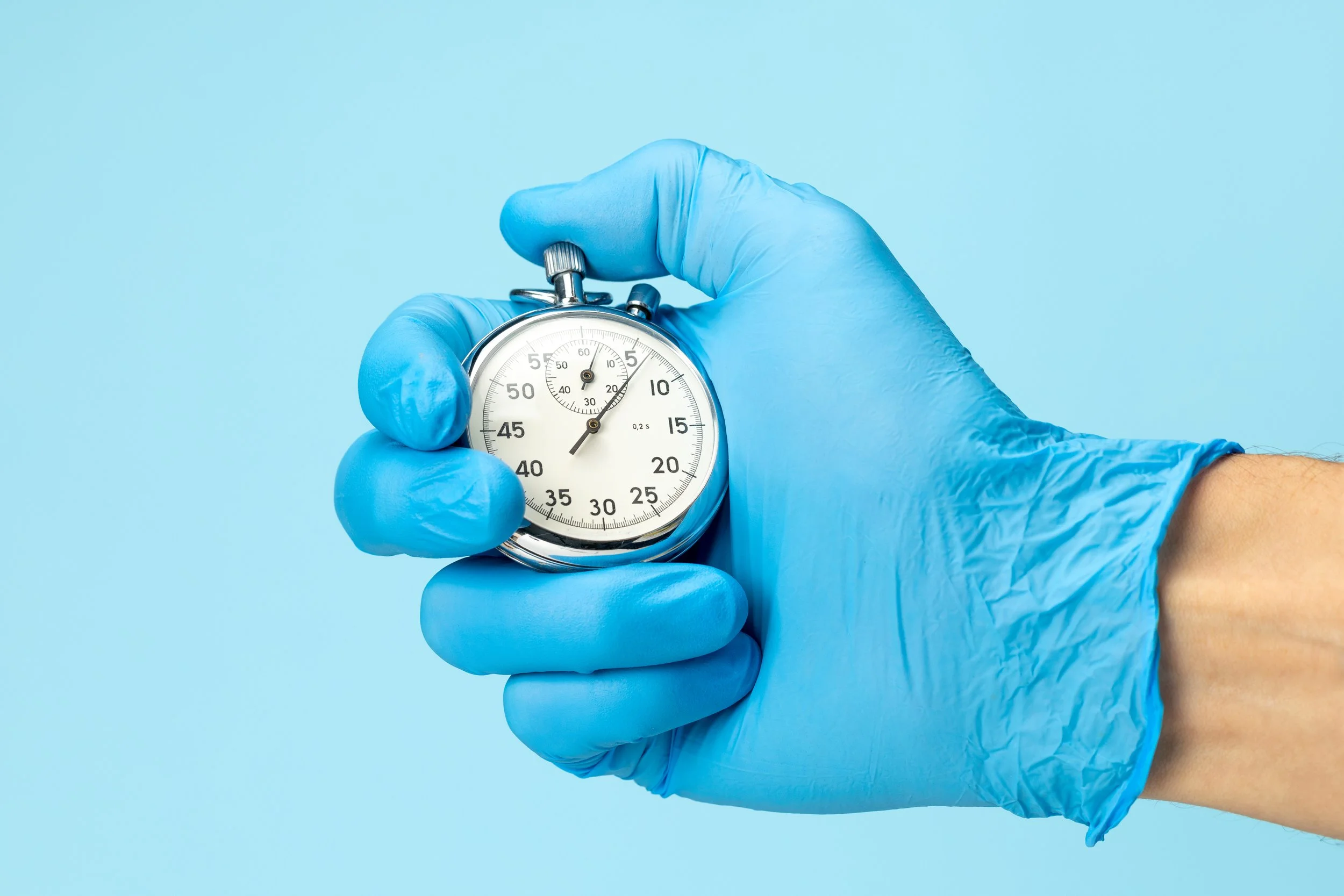 Hand in blue glove holding a stopwatch on a light blue background.