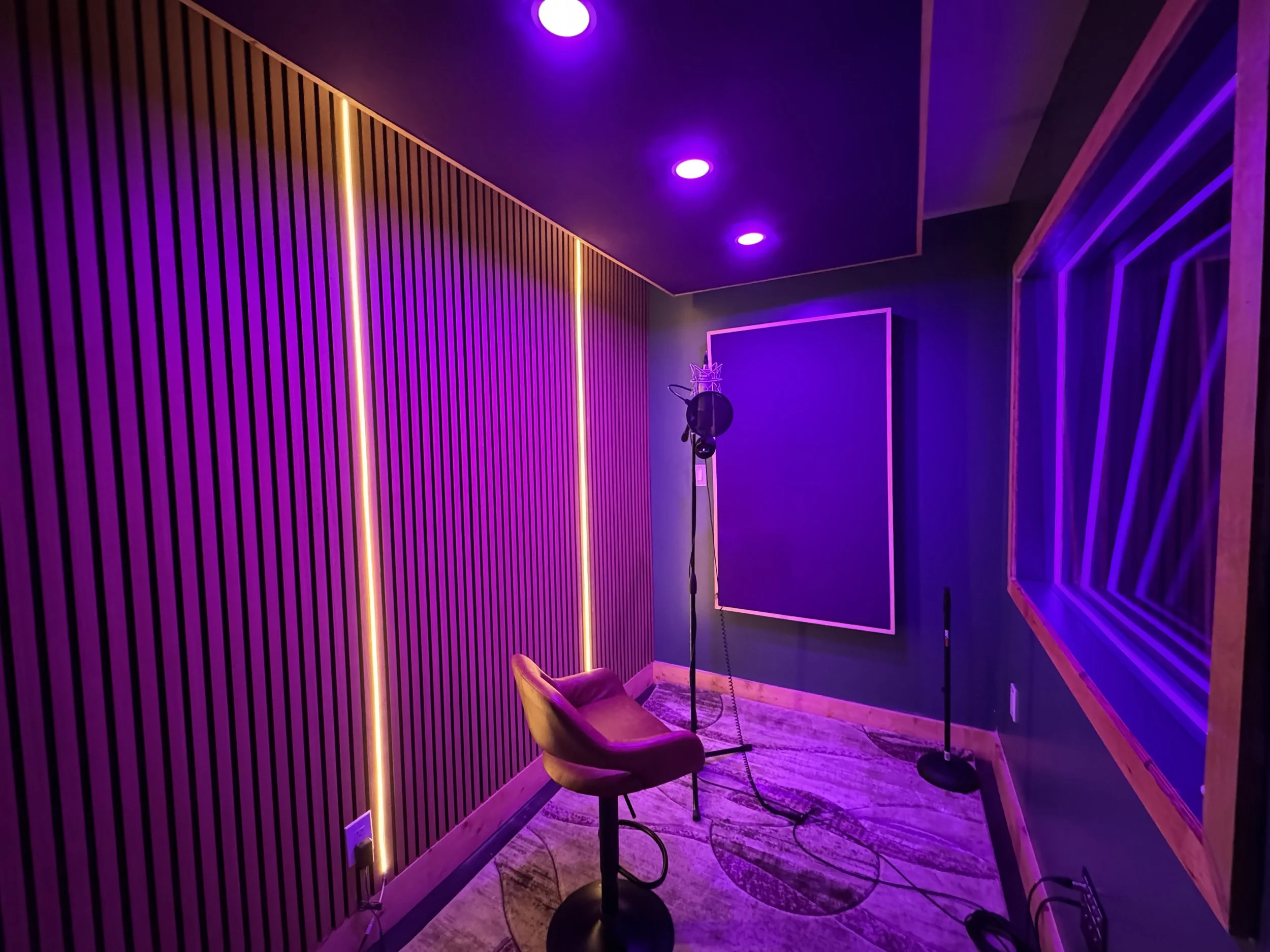 Music recording studio with purple lighting, featuring a microphone on a stand, a pop filter, a chair, and an acoustic panel on the wall.