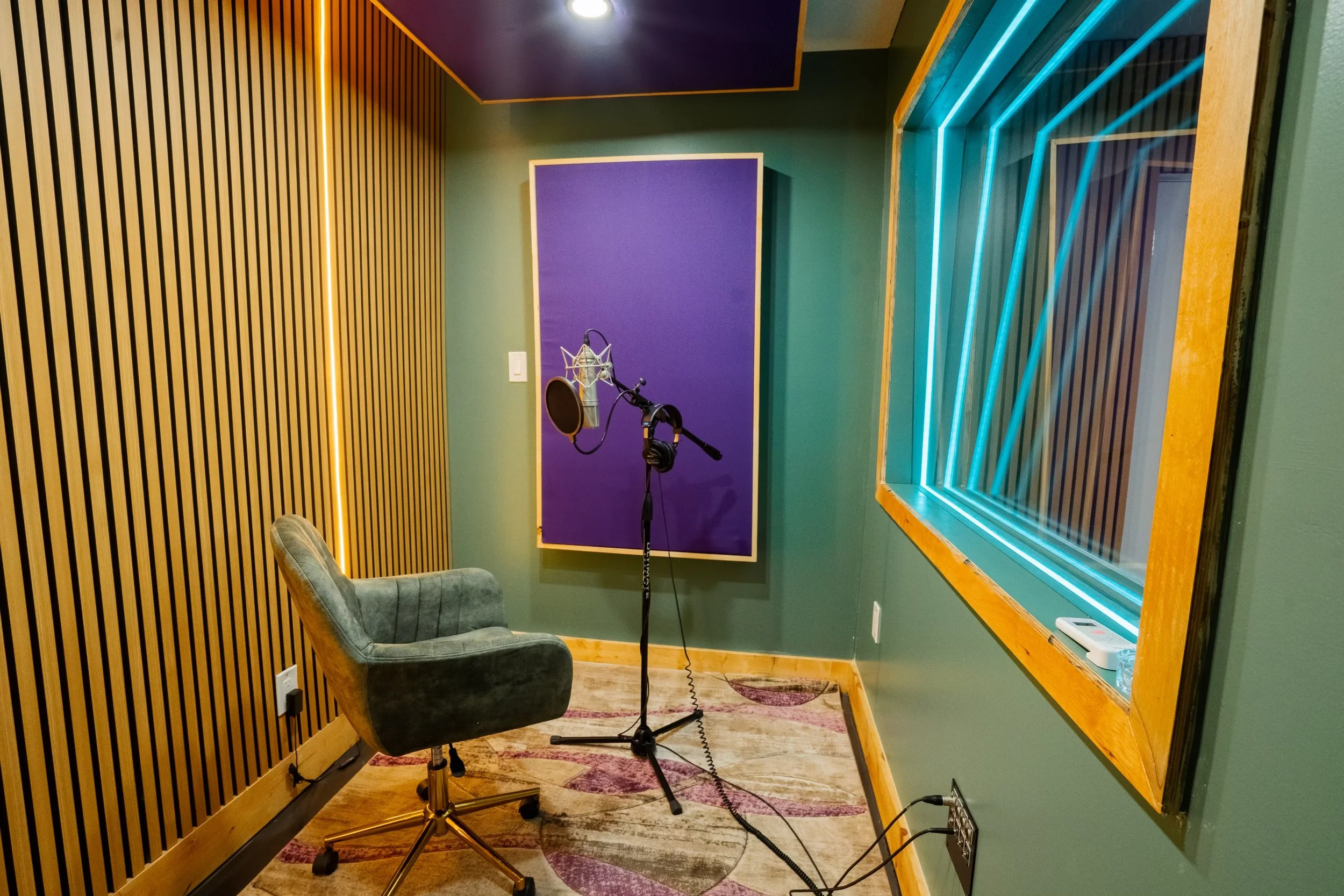 Recording studio booth with microphone, chair, and acoustic panel.
