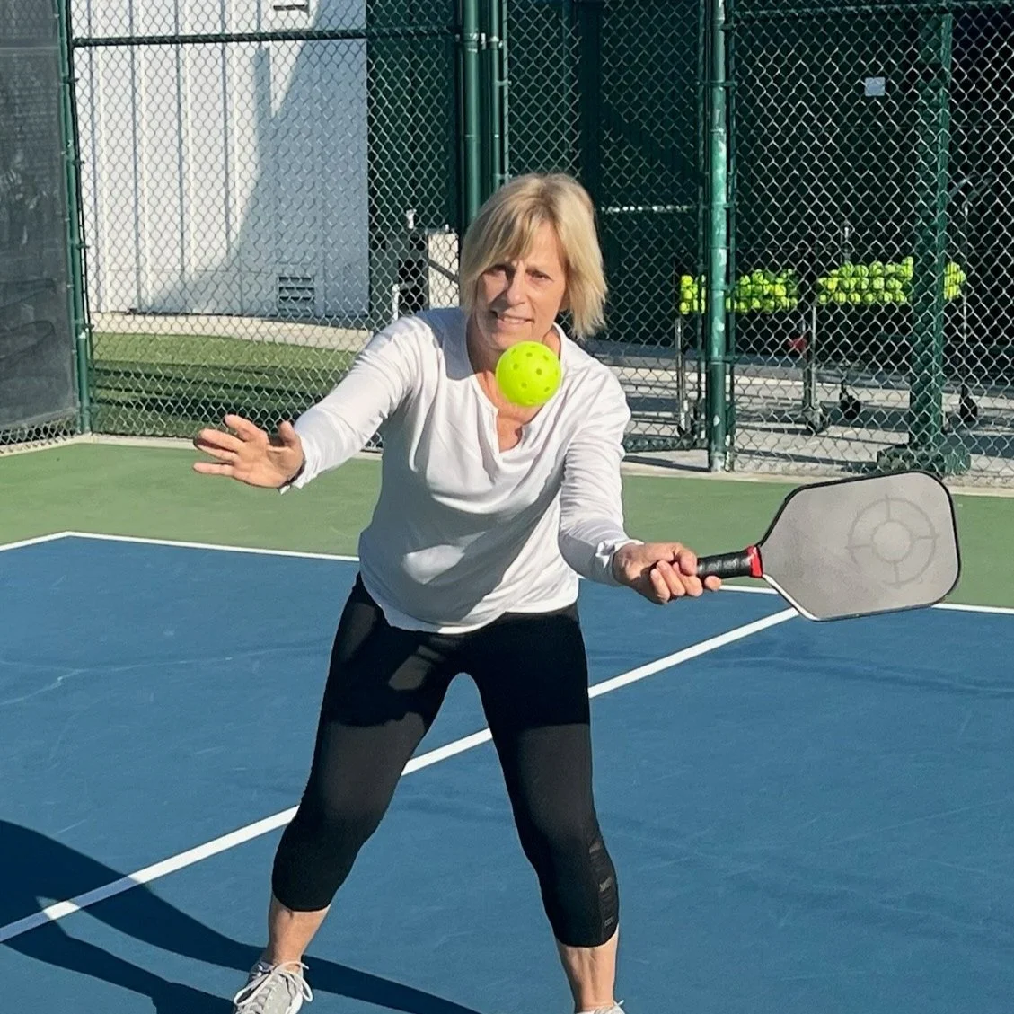 Person playing pickleball on a court with a paddle and ball.
