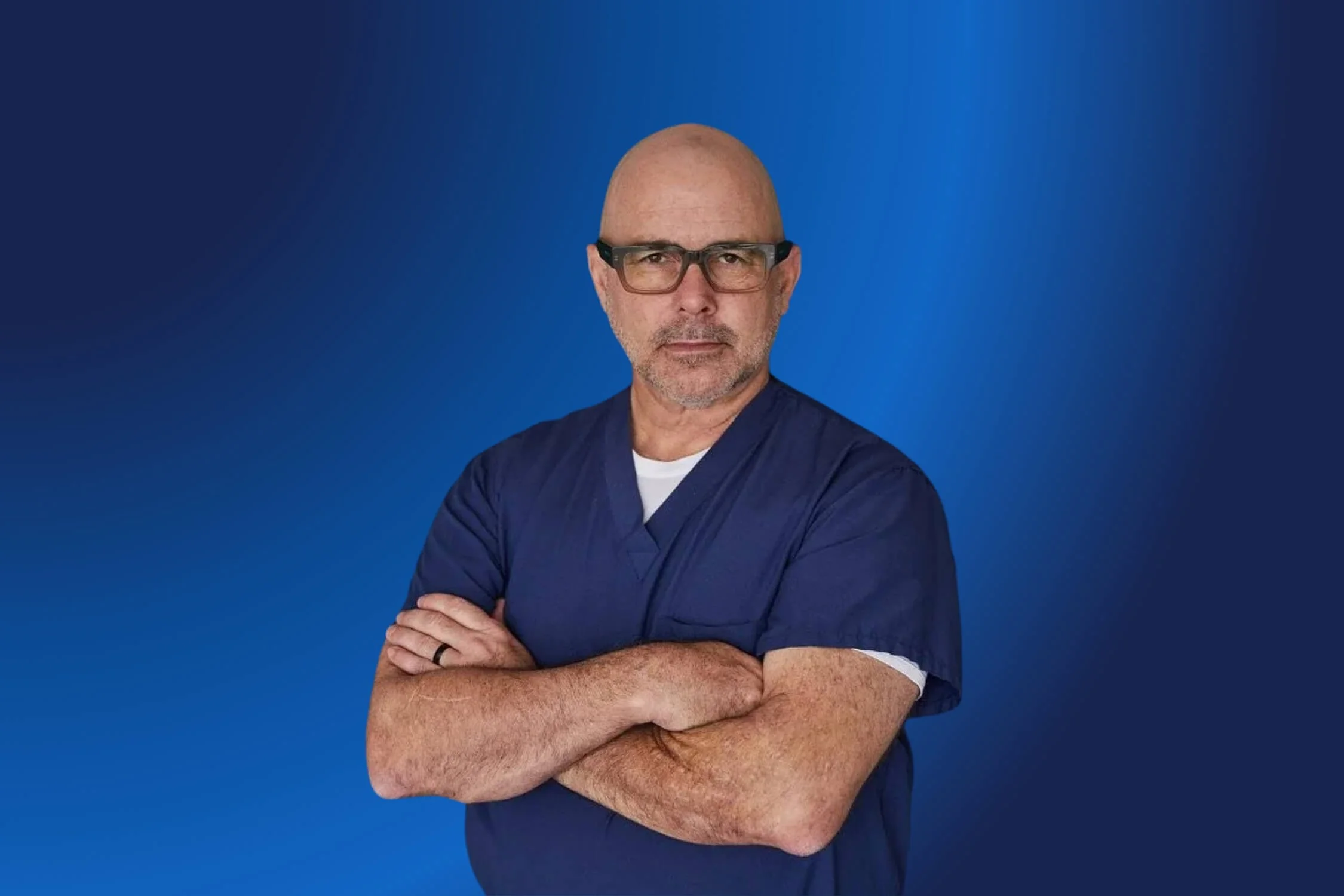 Joe Bellezzo with arms crossed wearing blue scrubs.
