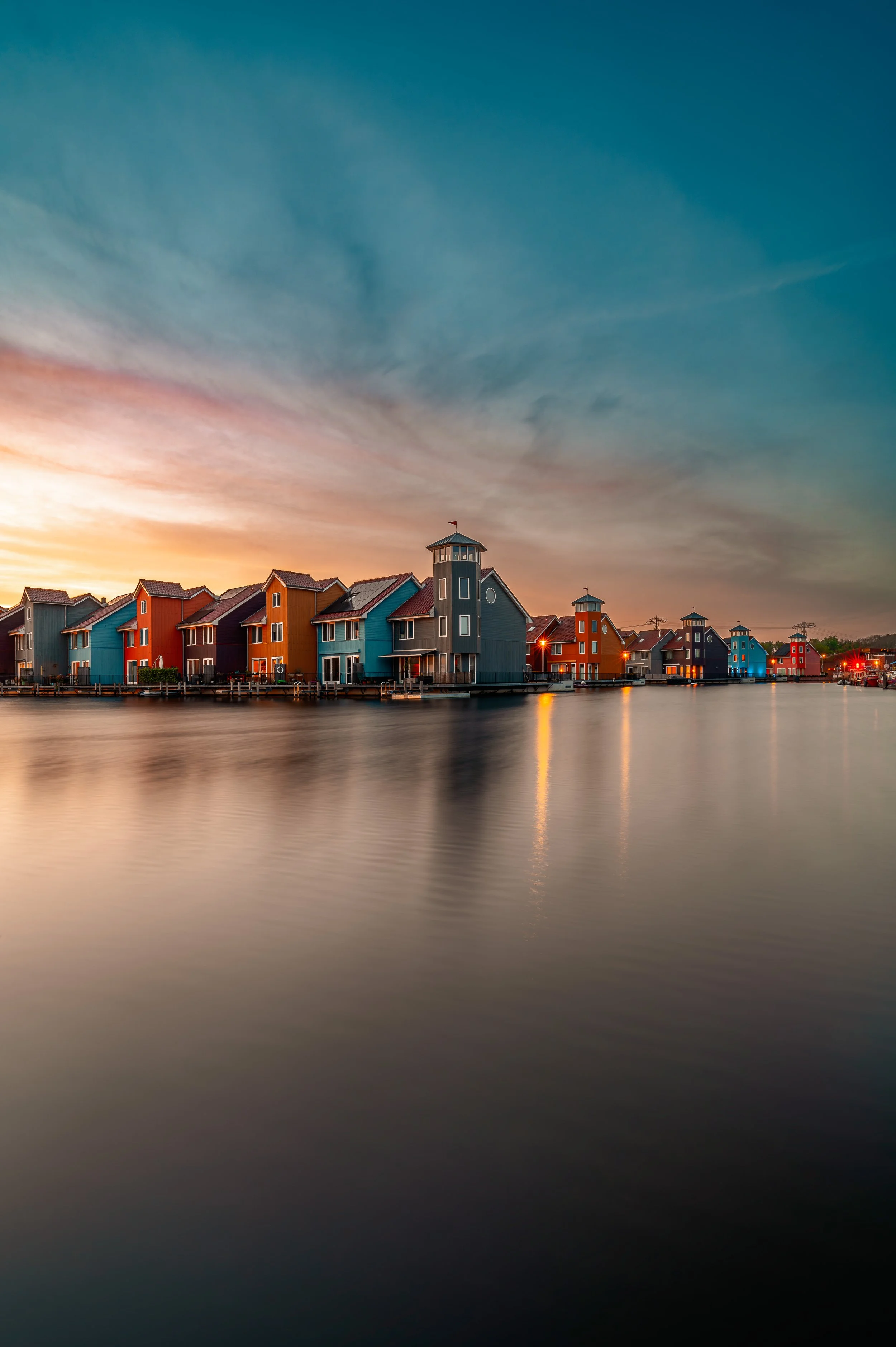 Colorful houses along a waterway at sunset with reflections on the water and a partly cloudy sky.