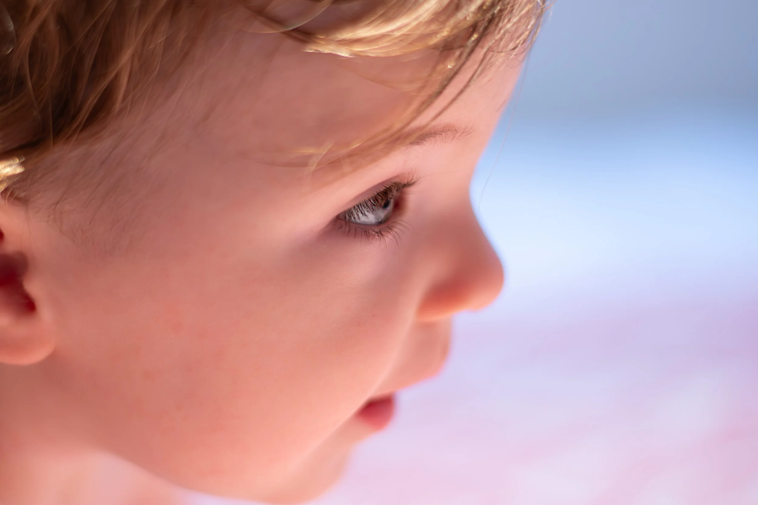 Close-up of a young child's face in profile with blonde hair and blue eyes, showing a soft expression.