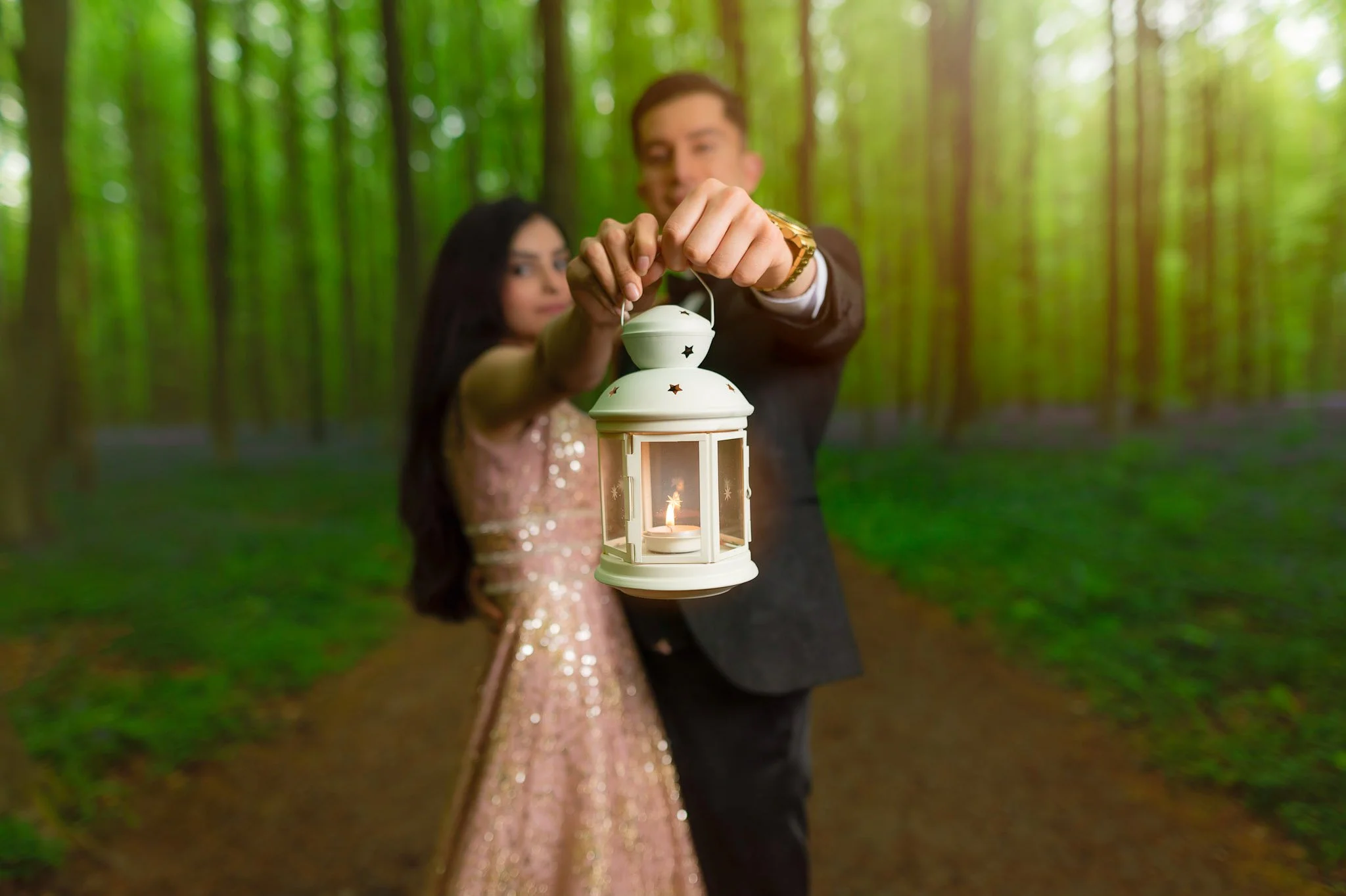 A couple dressed in formal attire holding a lit lantern together in a forest setting.