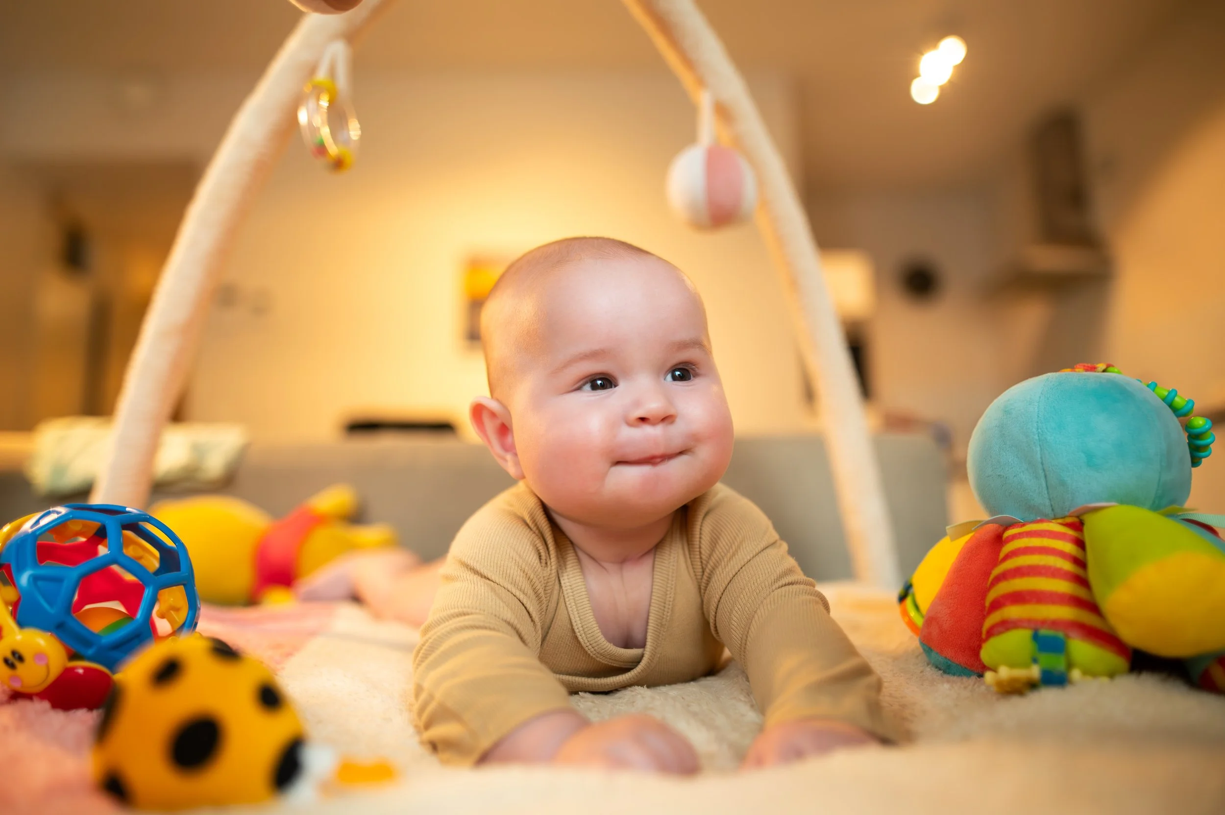 Baby crawling on a plush play mat surrounded by colorful toys, in a cozy living room environment.