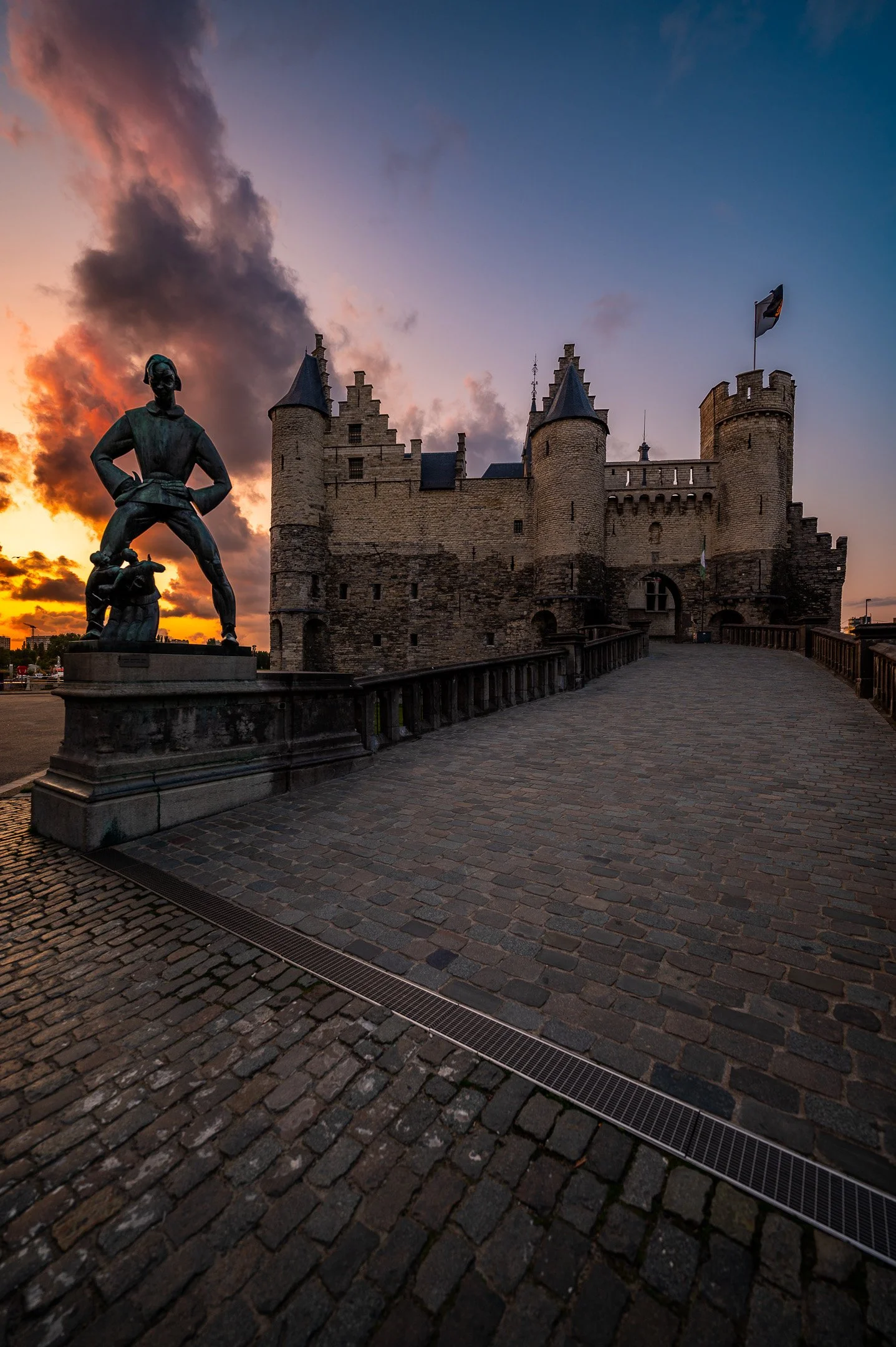 A stone castle with turrets at sunset, featuring a statue of a man in a dynamic pose in the foreground.