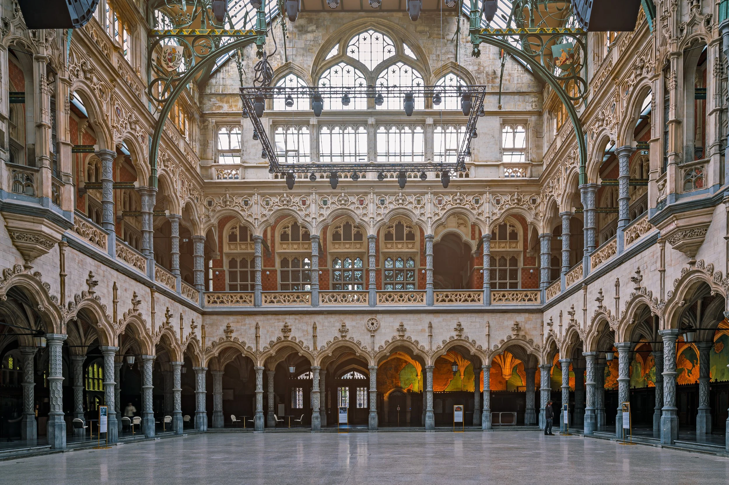 Interior of a historic building with ornate gothic architecture, multiple arched windows, decorative columns, and a large open floor space.
