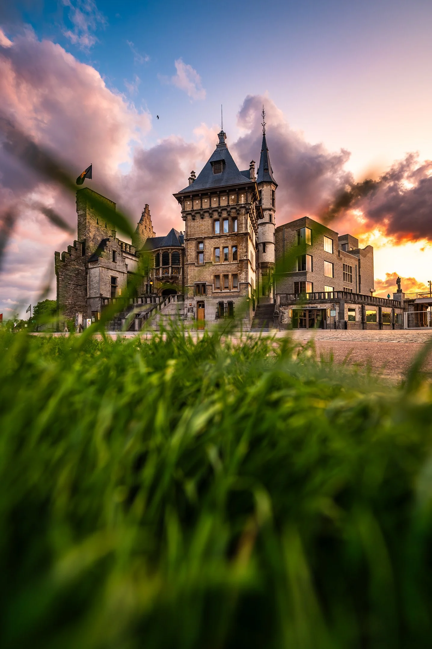 A large, old castle with multiple towers and turrets, set against a dramatic sunset sky with colorful clouds.