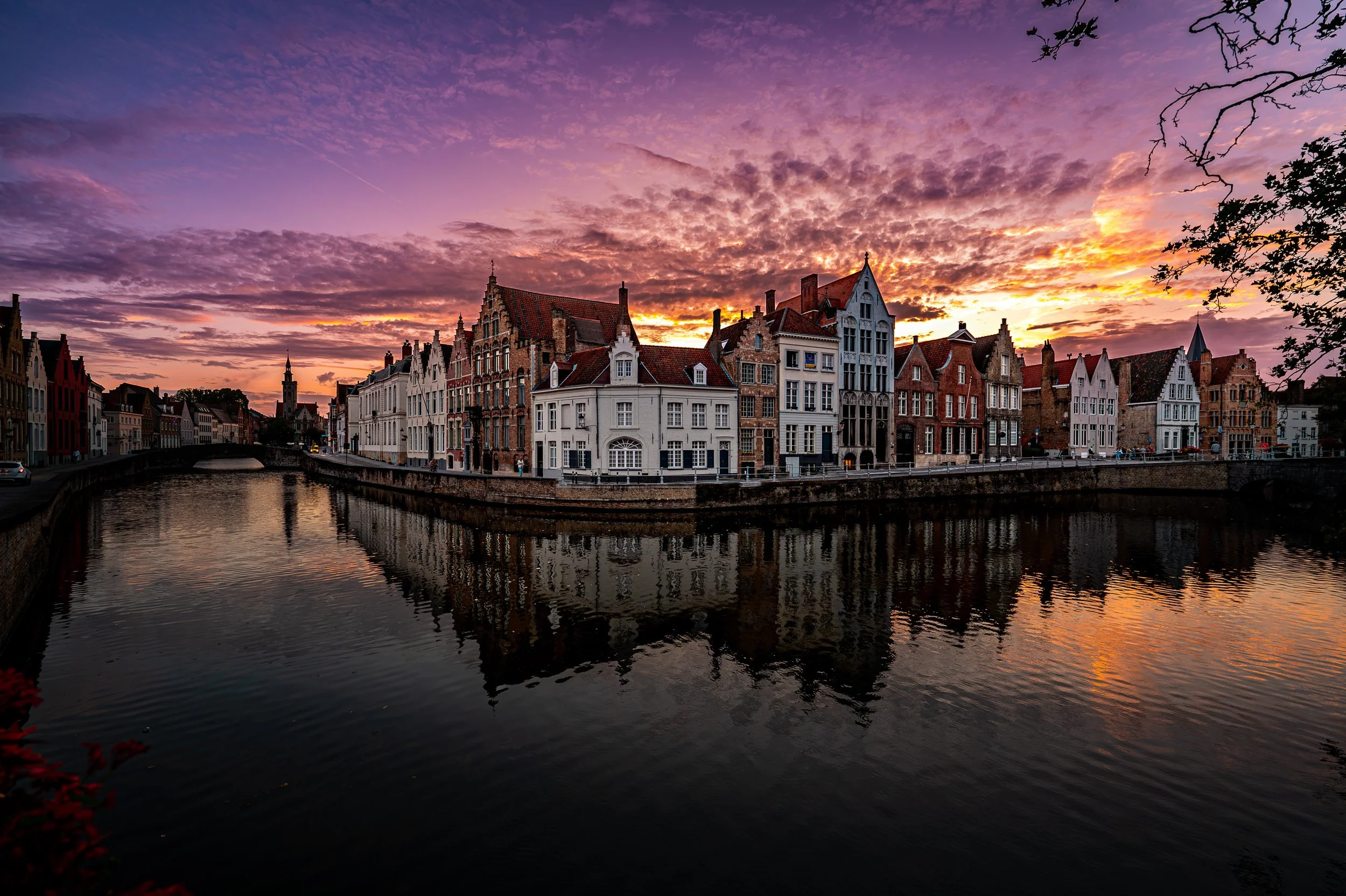 Scenic view of historic European-style buildings along a river at sunset with colorful sky and reflections in the water.