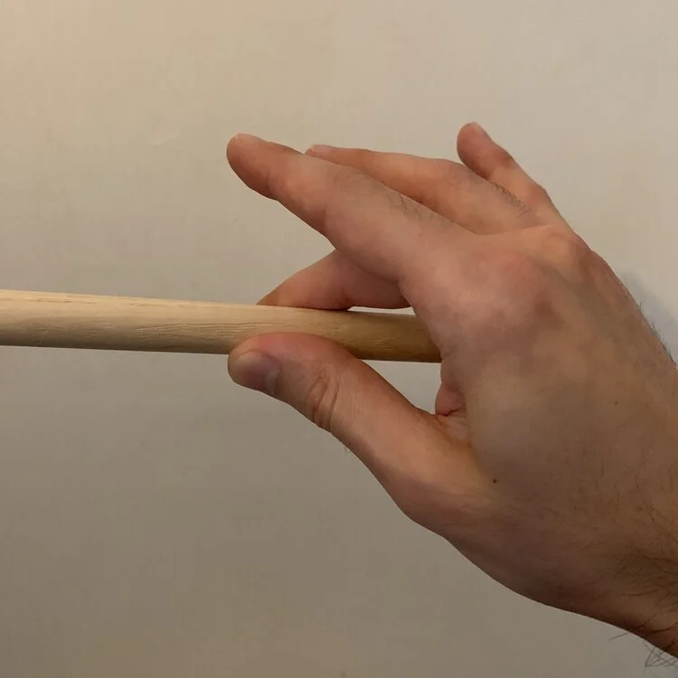 A hand holding a drum stick with the thumb and middle finger.