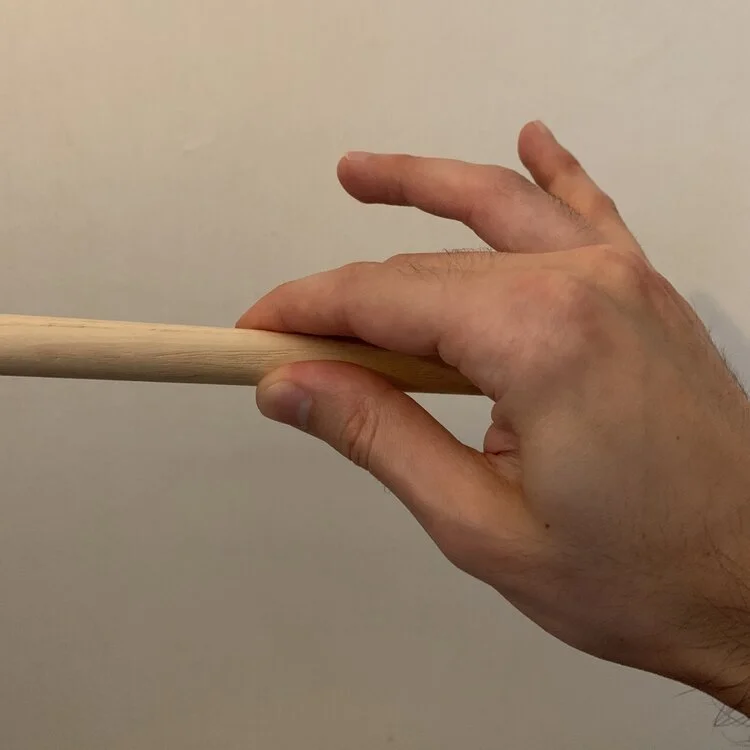 A hand holding a drum stick with the thumb, index, and middle fingers.