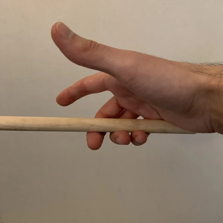 A hand holding a drum stick with the middle, ring, and pinkie fingers.