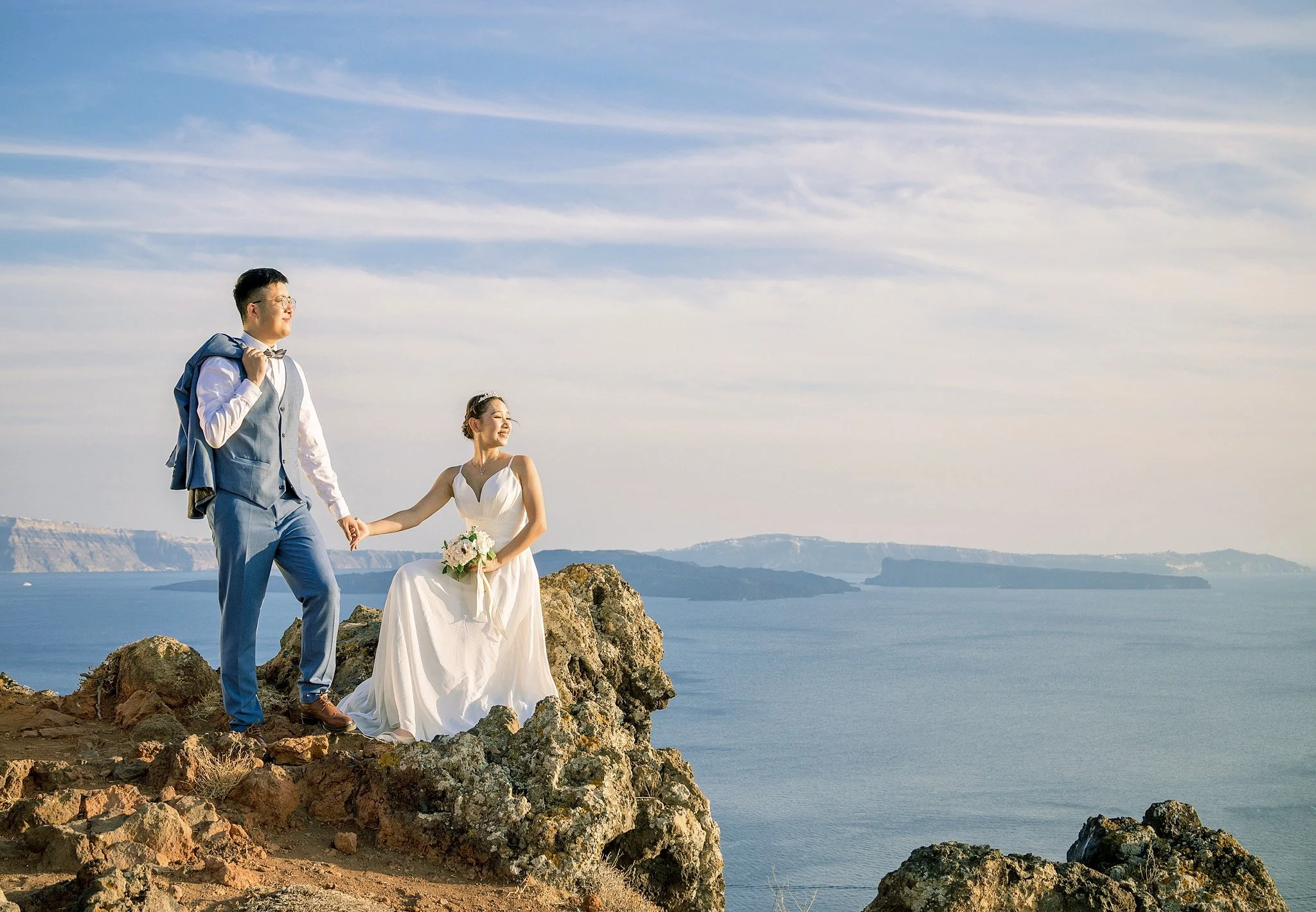 Family portraits on Santorini cliffs with blue-domed church in background, celebrating love under twilight sky during Pregnancy glow.
