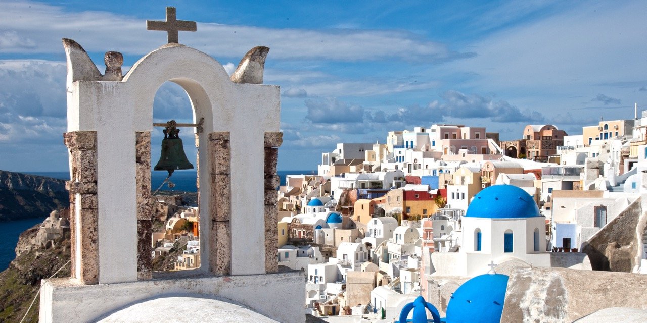 Crowds and photographers watching the famous Santorini sunset from Oia Castle ruins with fiery colors reflecting on the caldera.