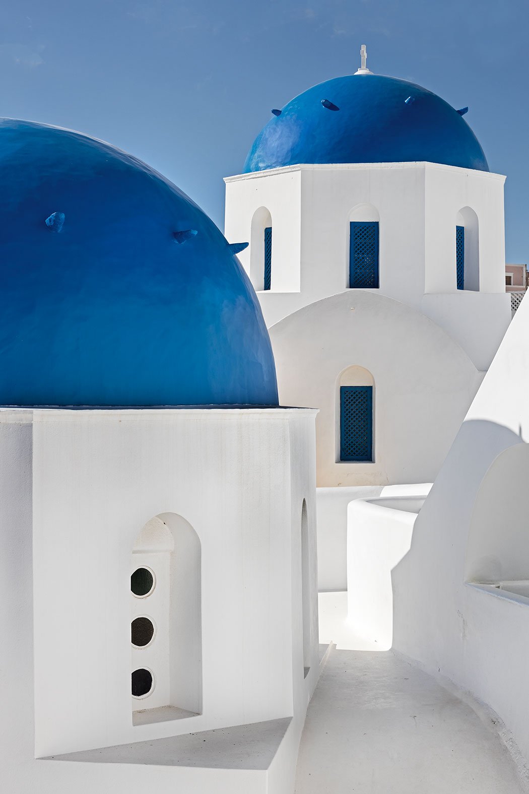 Narrow cobblestone streets of Fira lined with whitewashed houses and iconic blue-domed churches framed against a clear Santorini sky.