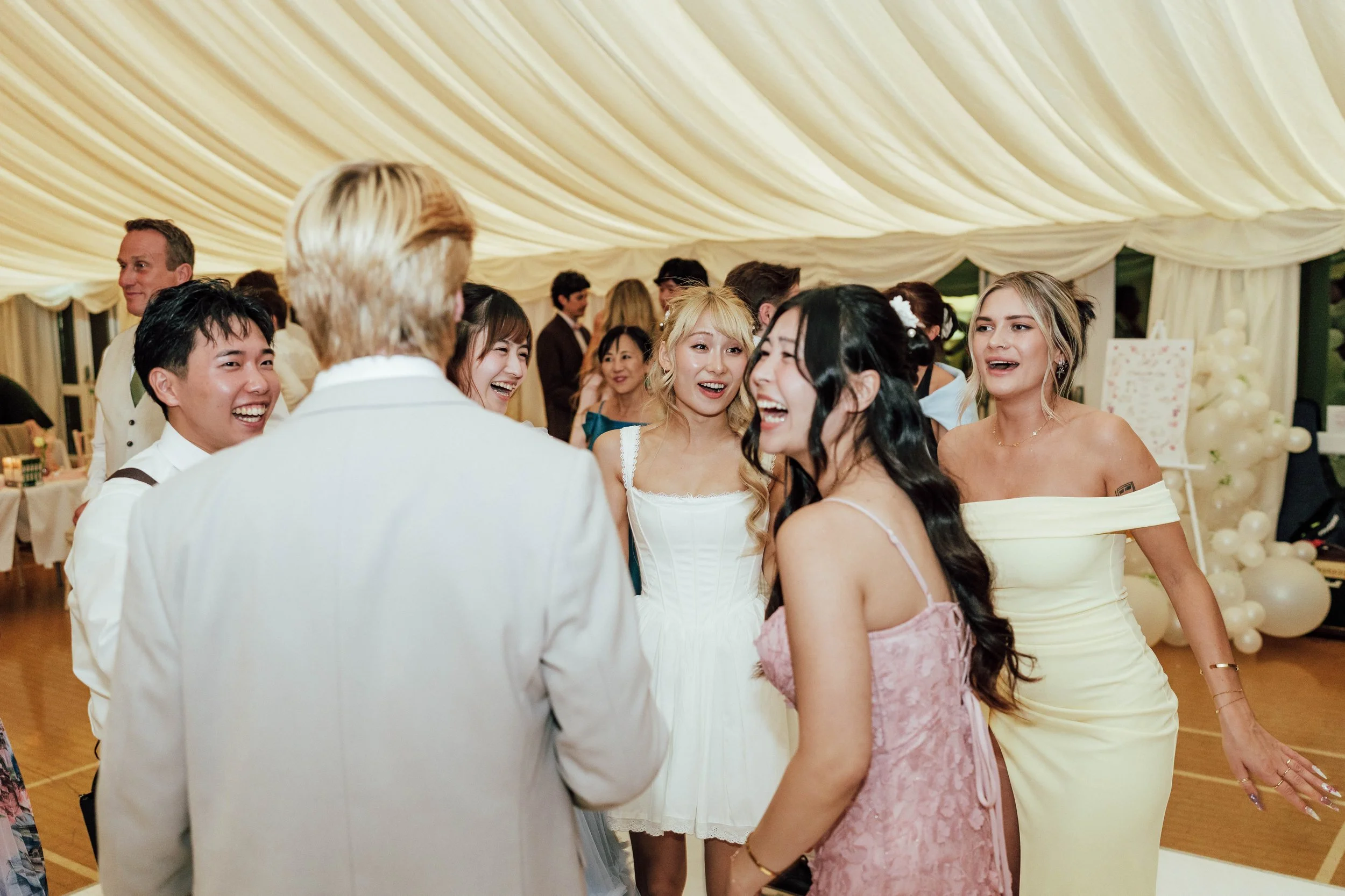 Group of women and men smiling and talking at a wedding reception in a decorated tent.