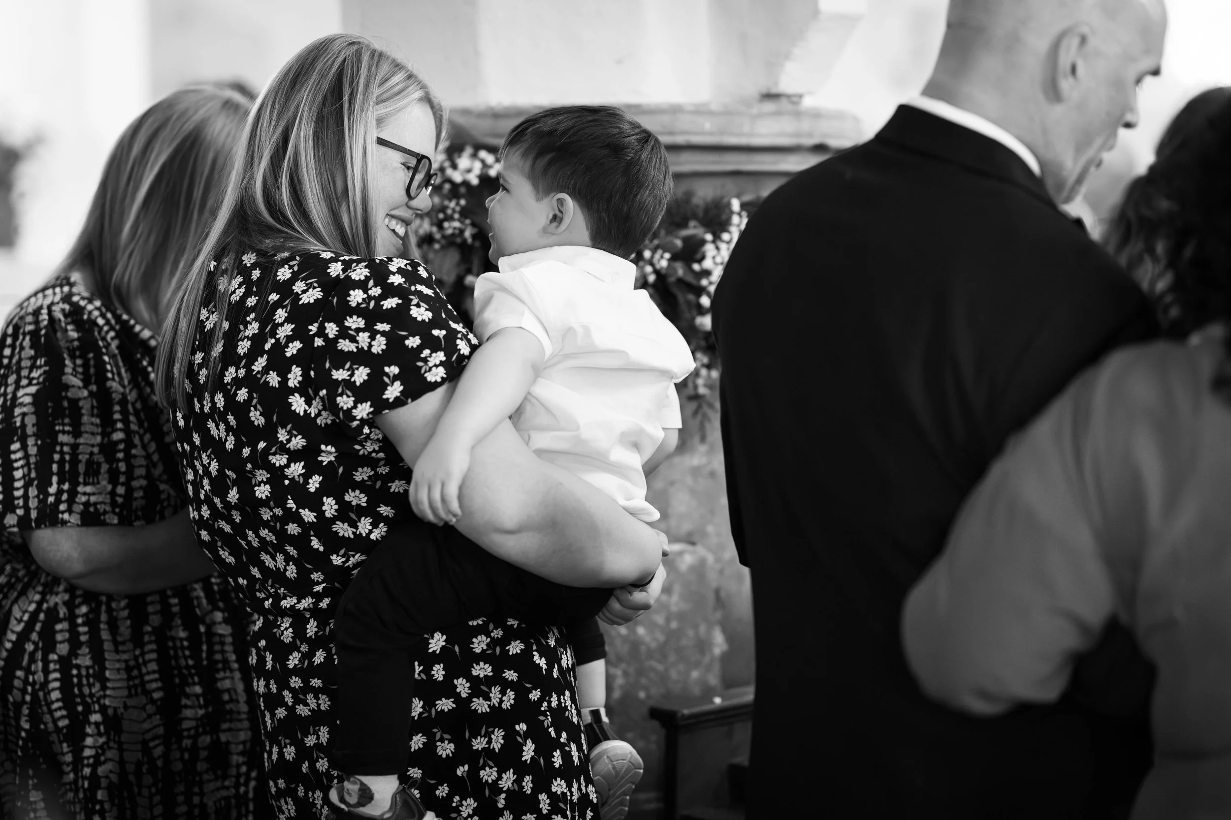 A woman holding a young boy, smiling at each other, at what appears to be a social gathering or celebration.