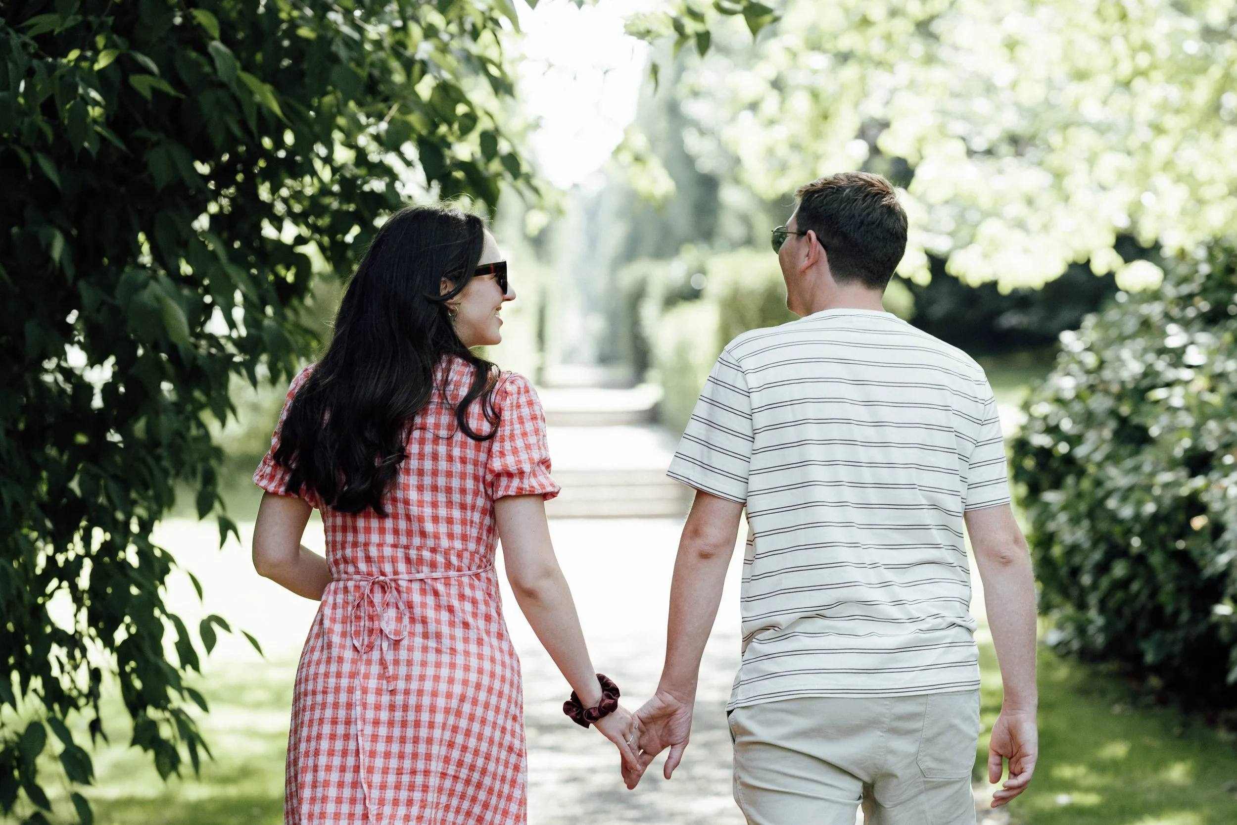 A couple holding hands and walking in a park with greenery.