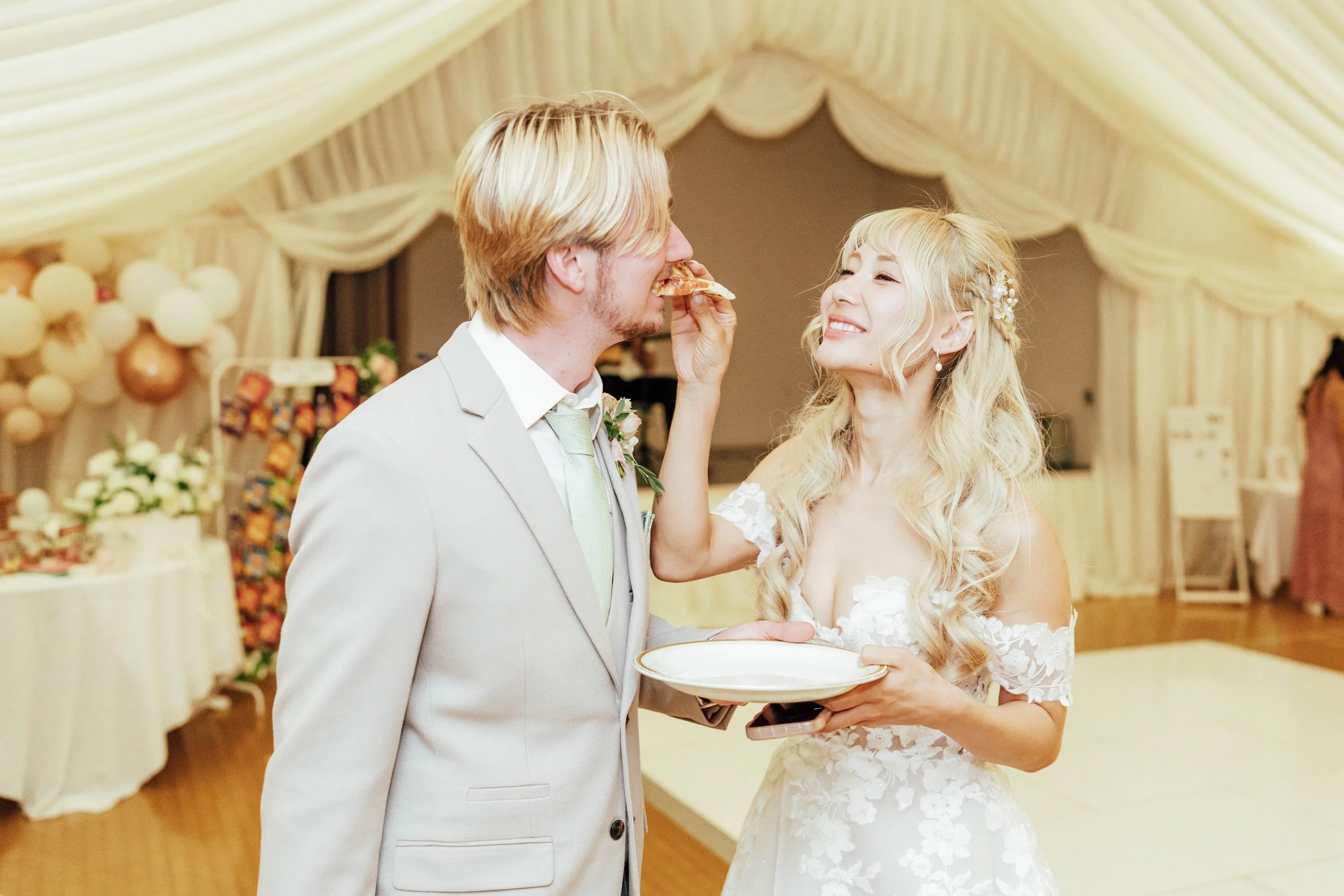 Bride playfully feeding a slice of pizza to groom during wedding celebration in decorated venue.
