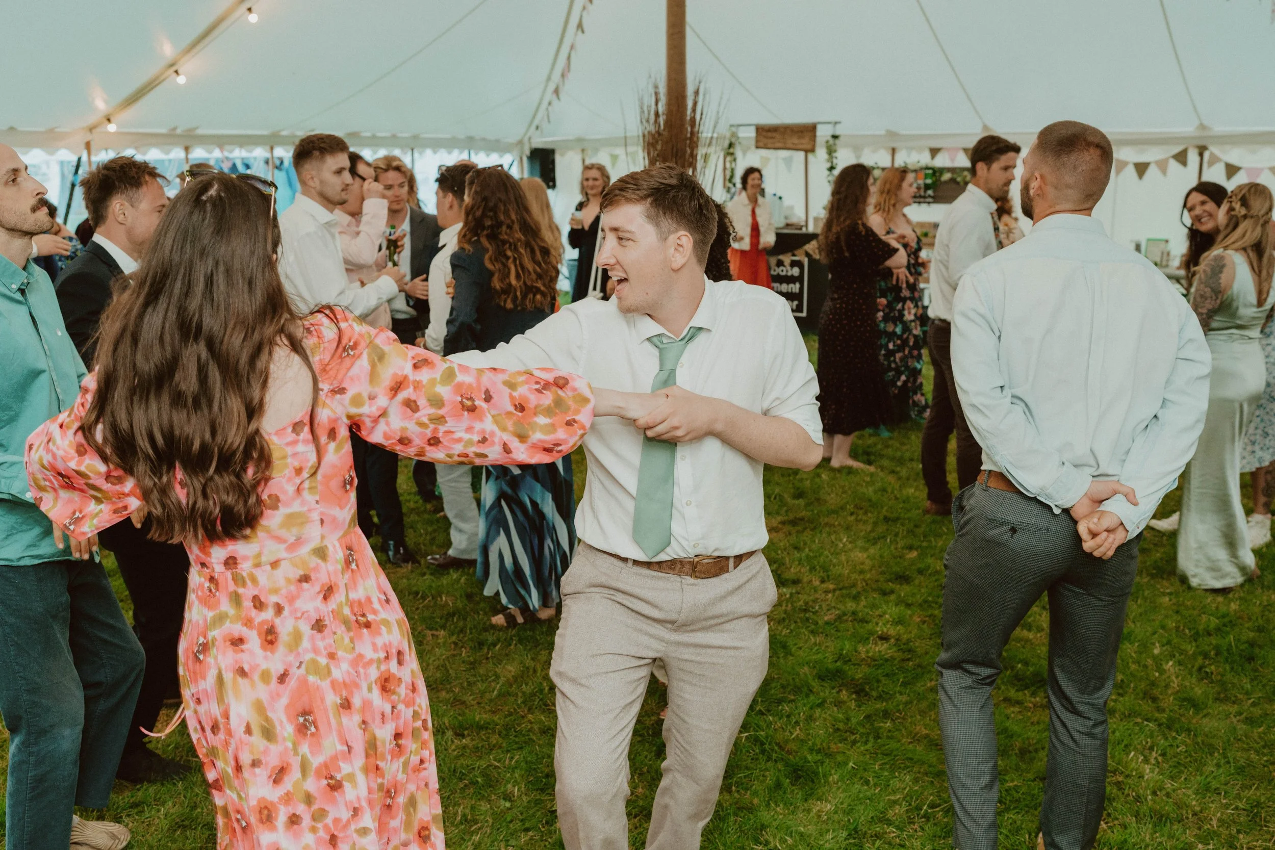 People dancing and socializing inside a large white tent at a celebration or wedding.