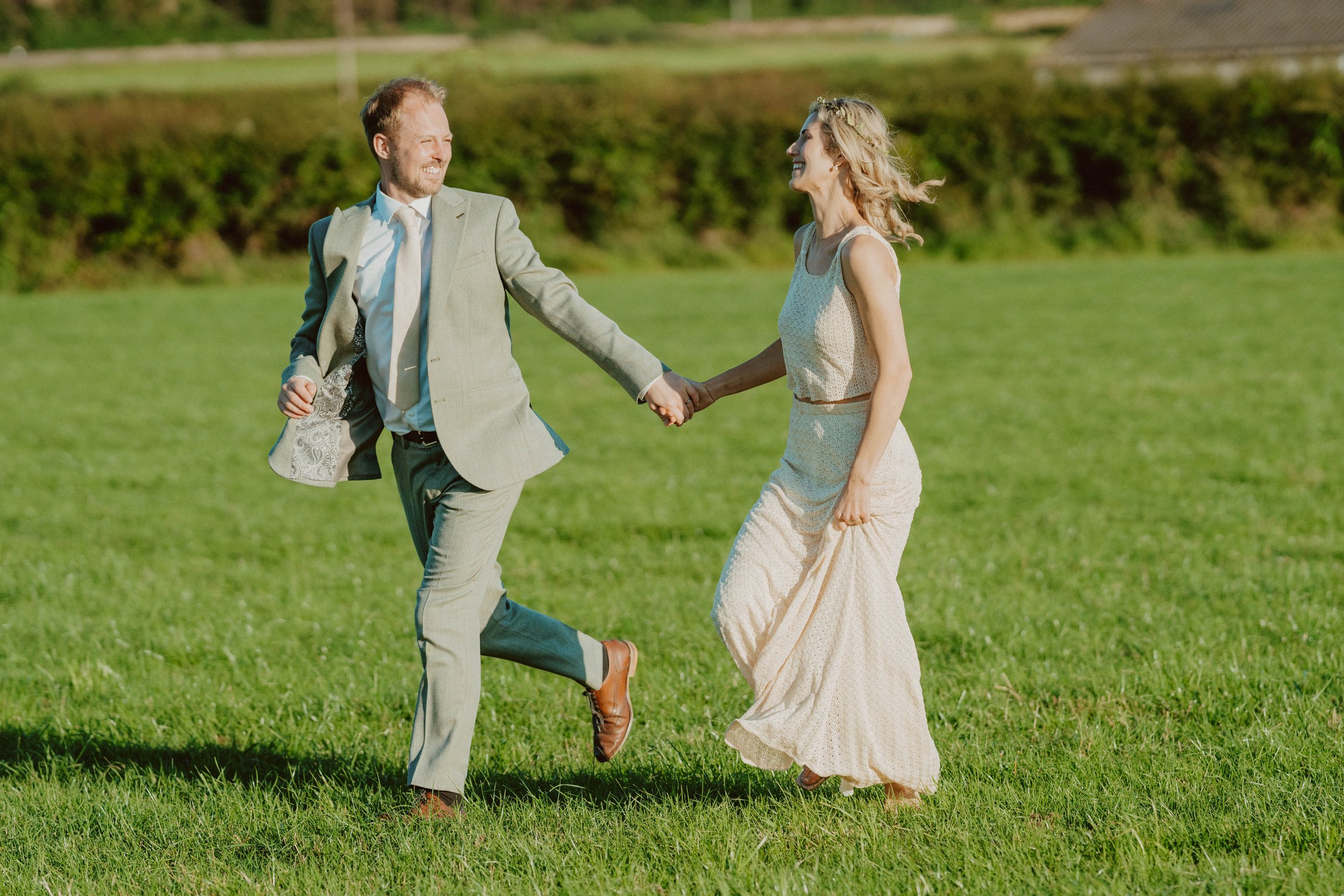 A smiling man and woman holding hands and running across a grassy field during daytime.