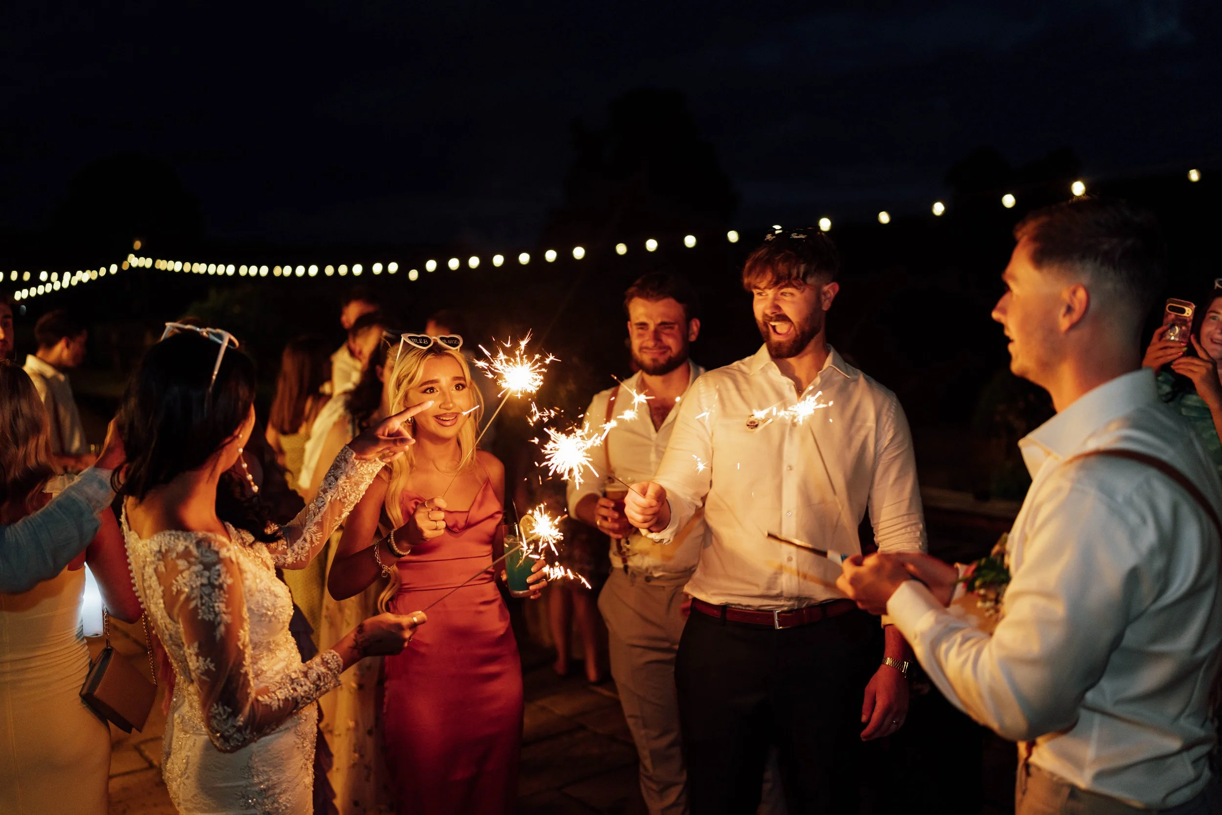 Group of people celebrating with sparklers at night, outdoor party, smiling and taking photos.