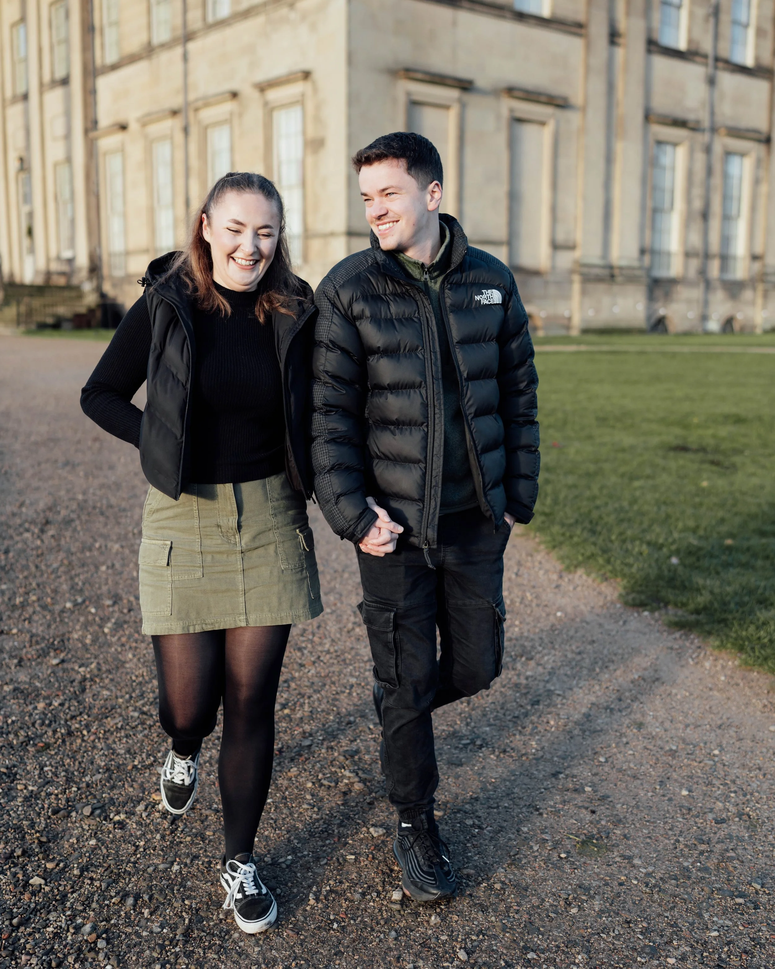 A young couple walking hand in hand outdoors near a historic building, smiling and enjoying each other's company.