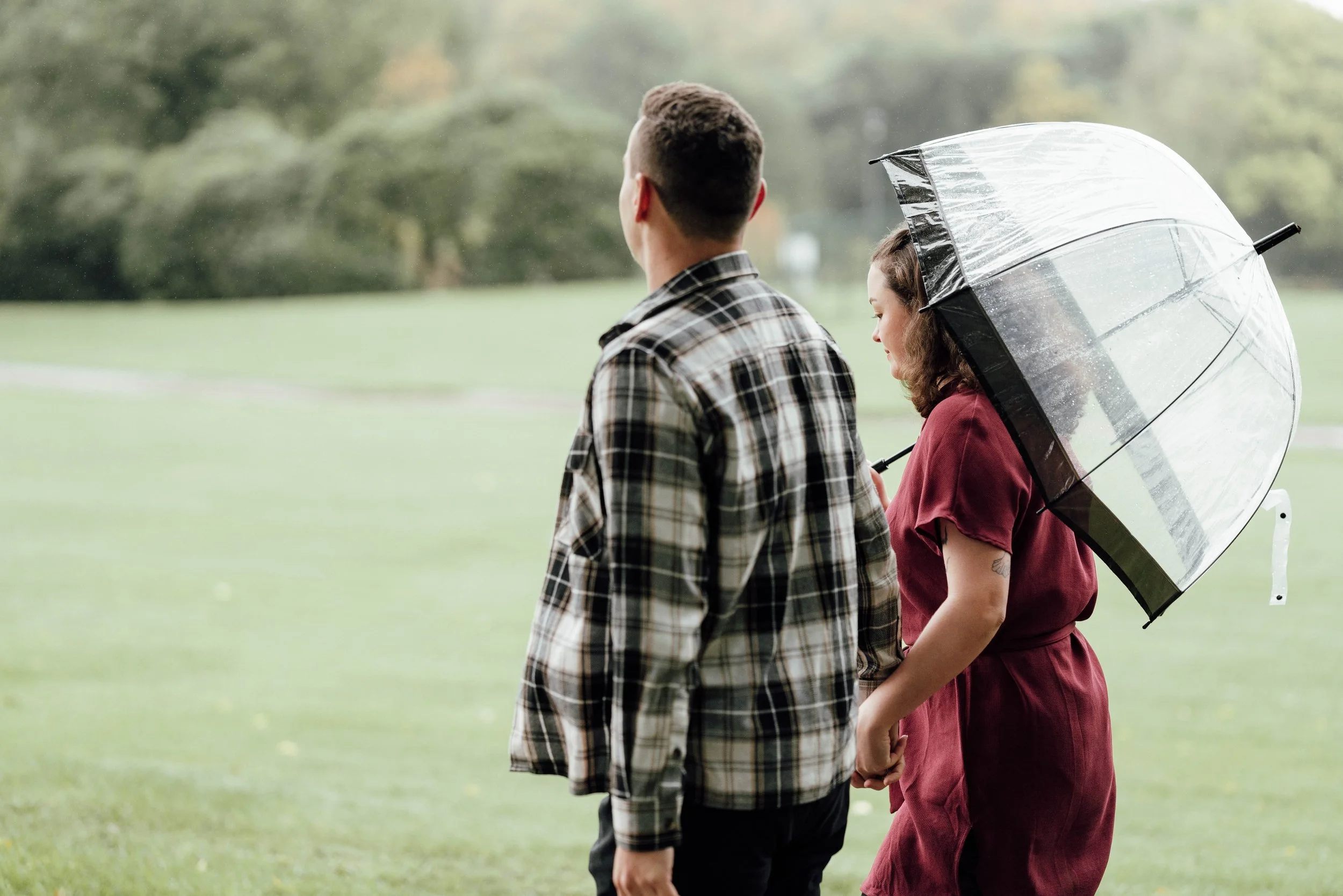 A couple walking in a park on a rainy day, holding hands, with the woman holding an umbrella.