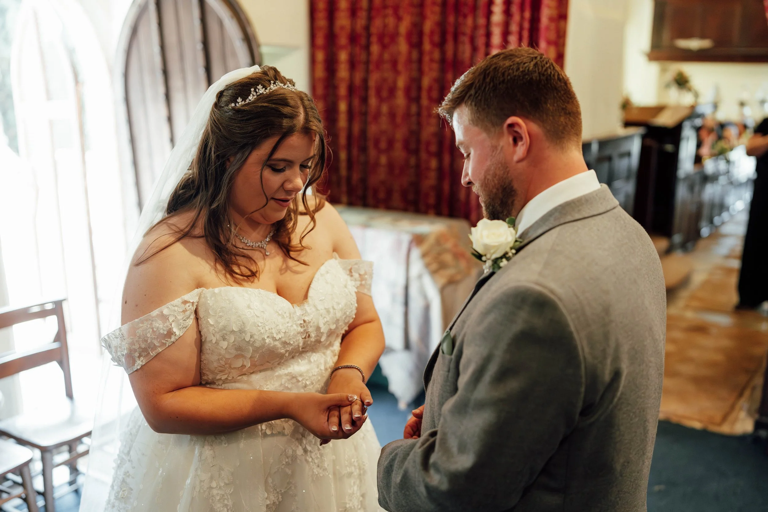 A bride and groom exchange vows indoors during a wedding ceremony, holding hands and looking at each other.