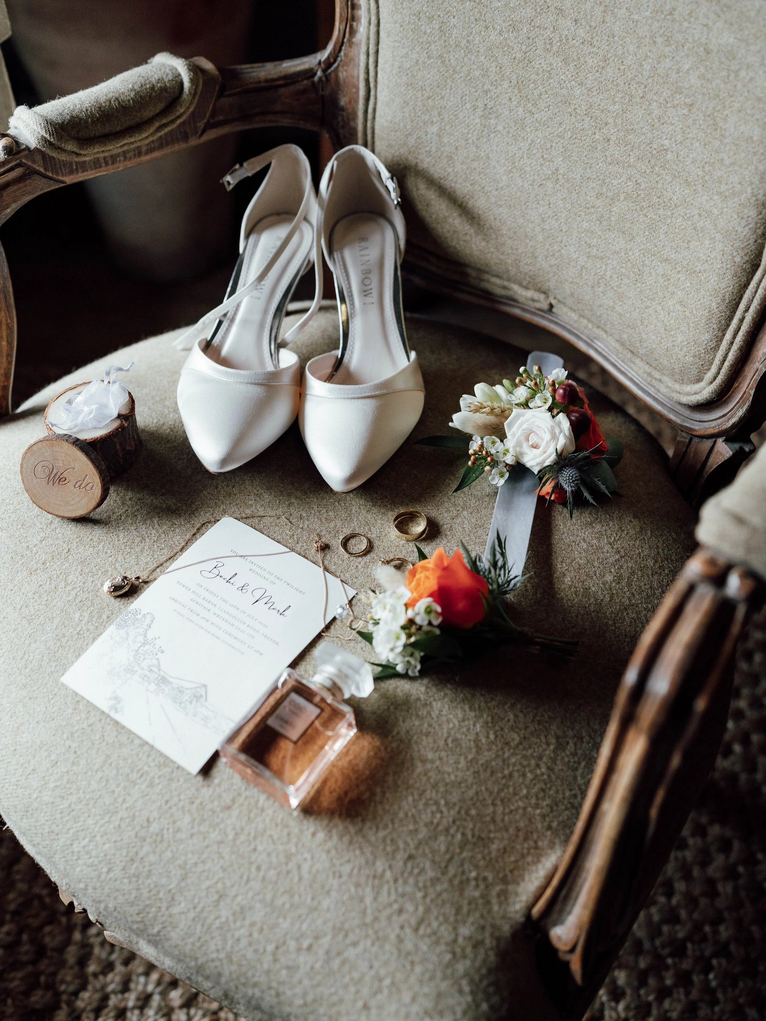 Wedding shoes, bouquet, rings, and invitation on a vintage chair.