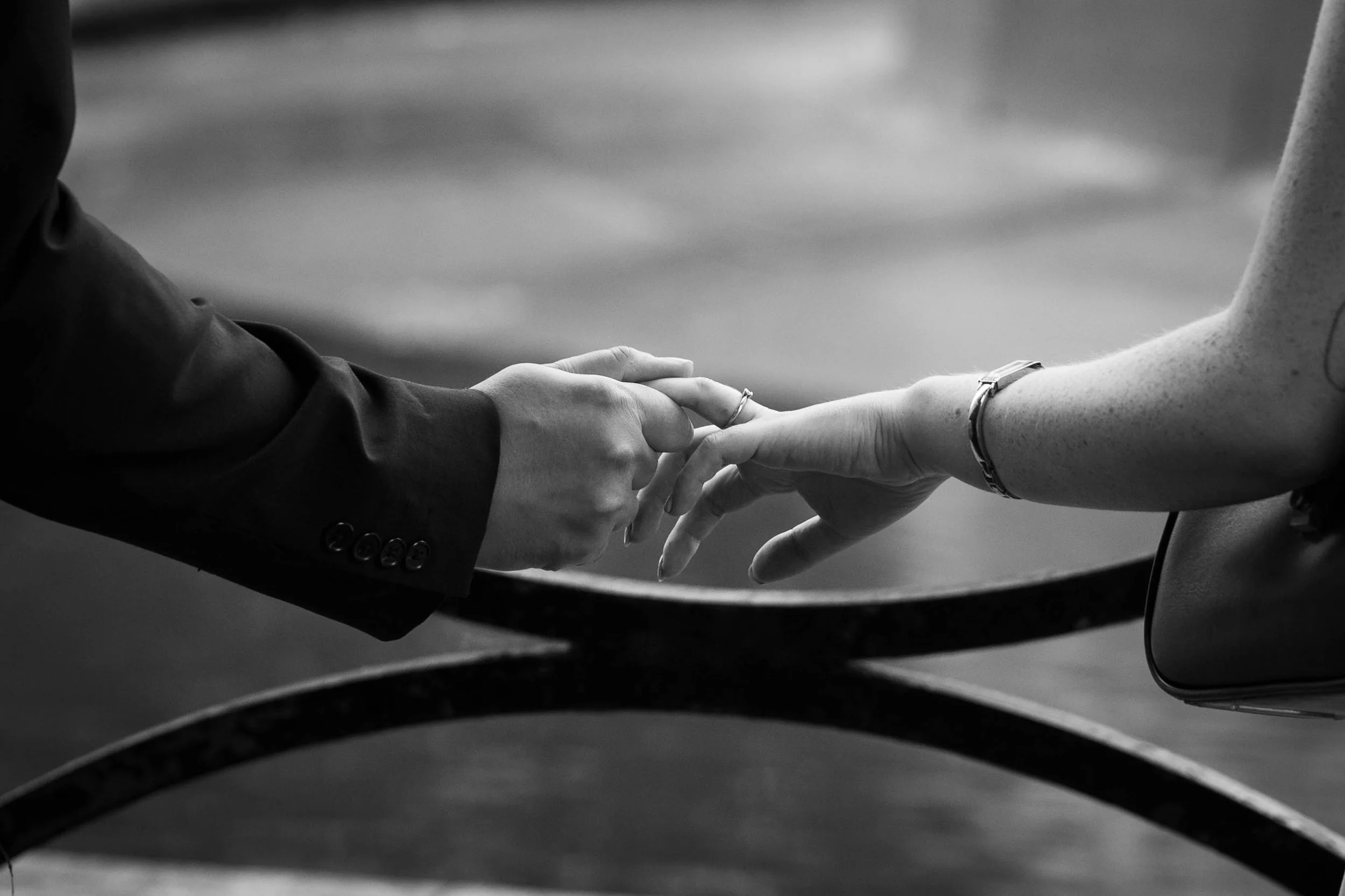 Two hands, one in a suit jacket, reaching out and touching fingertips with a person wearing a bracelet and a tank top.