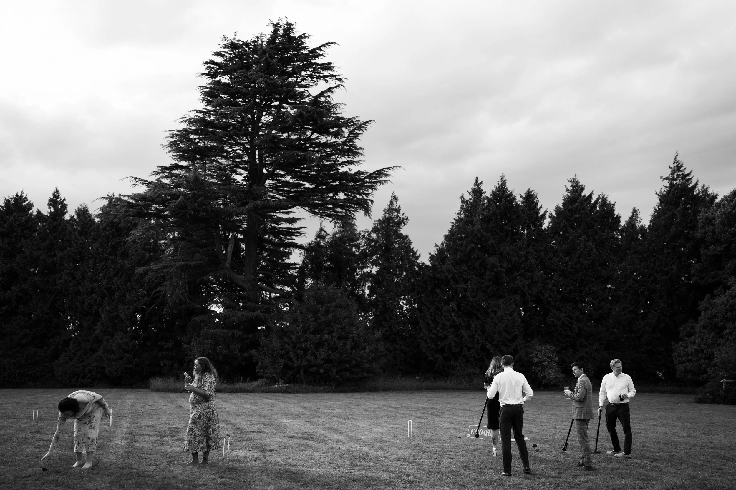 People playing croquet on a lawn with trees in the background, black and white image.