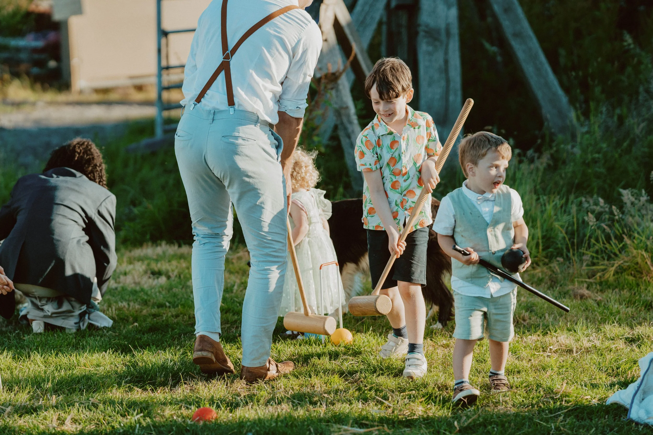 Children playing croquet outdoors on a sunny day with green grass and trees.