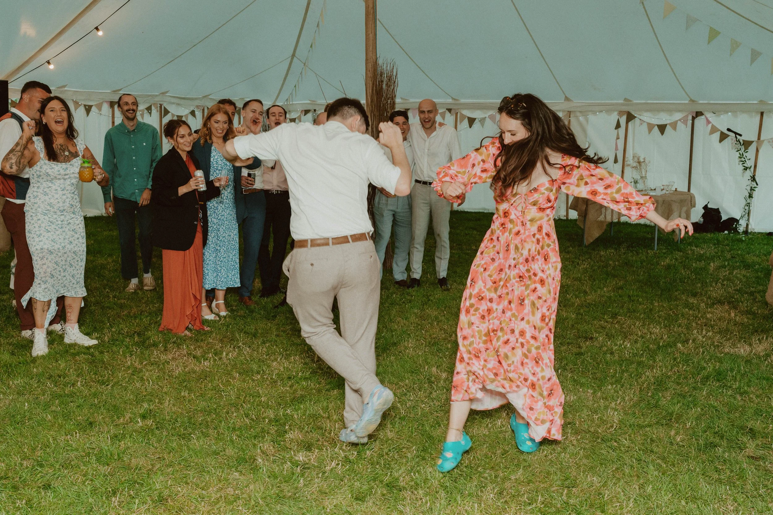 People dancing and having fun at a party under a large tent decorated with bunting.