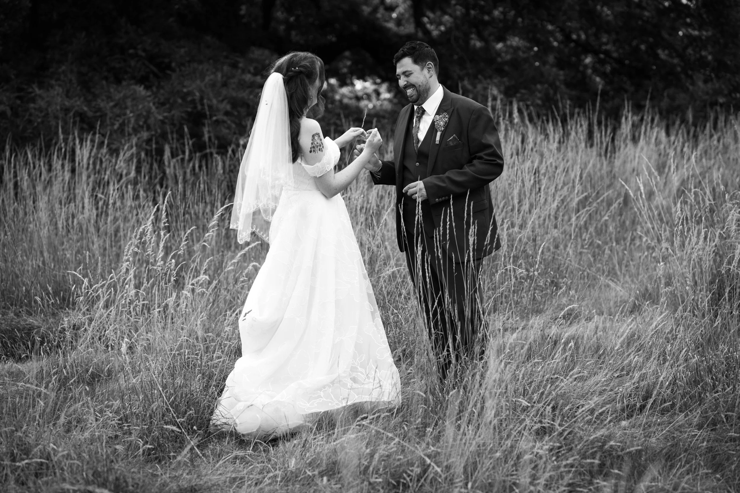 A bride and groom exchanging vows outdoors in a grassy field, black and white photograph.