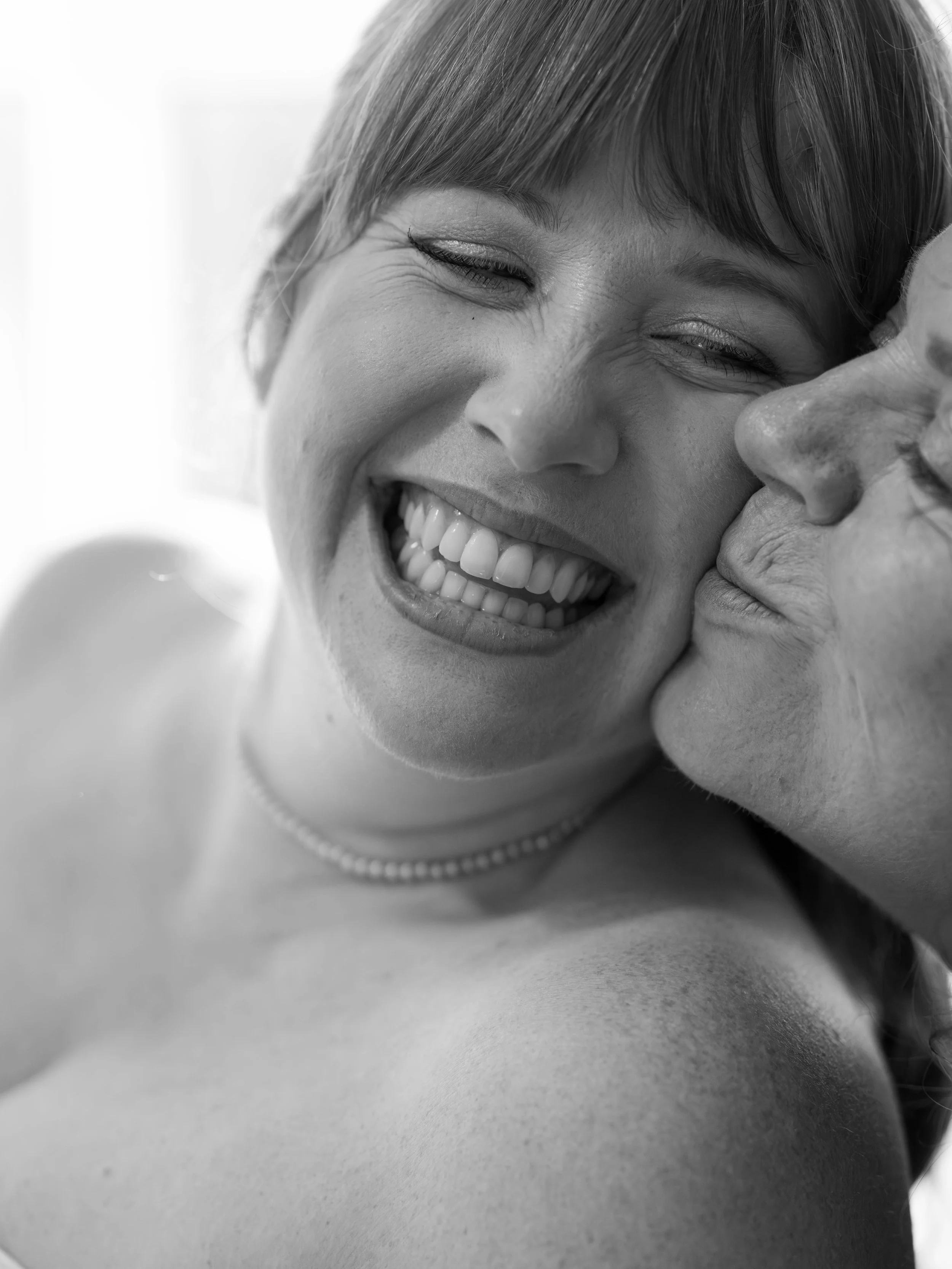 A woman laughing joyfully with an older woman kissing her cheek.